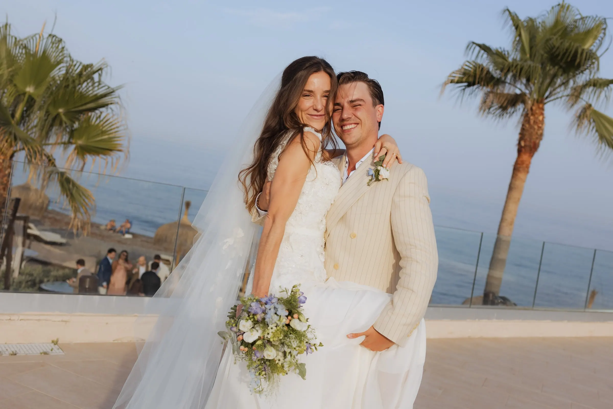 Bride leaning on the groom with her bouquet, palms and sea behind, Barbillón, Marbella