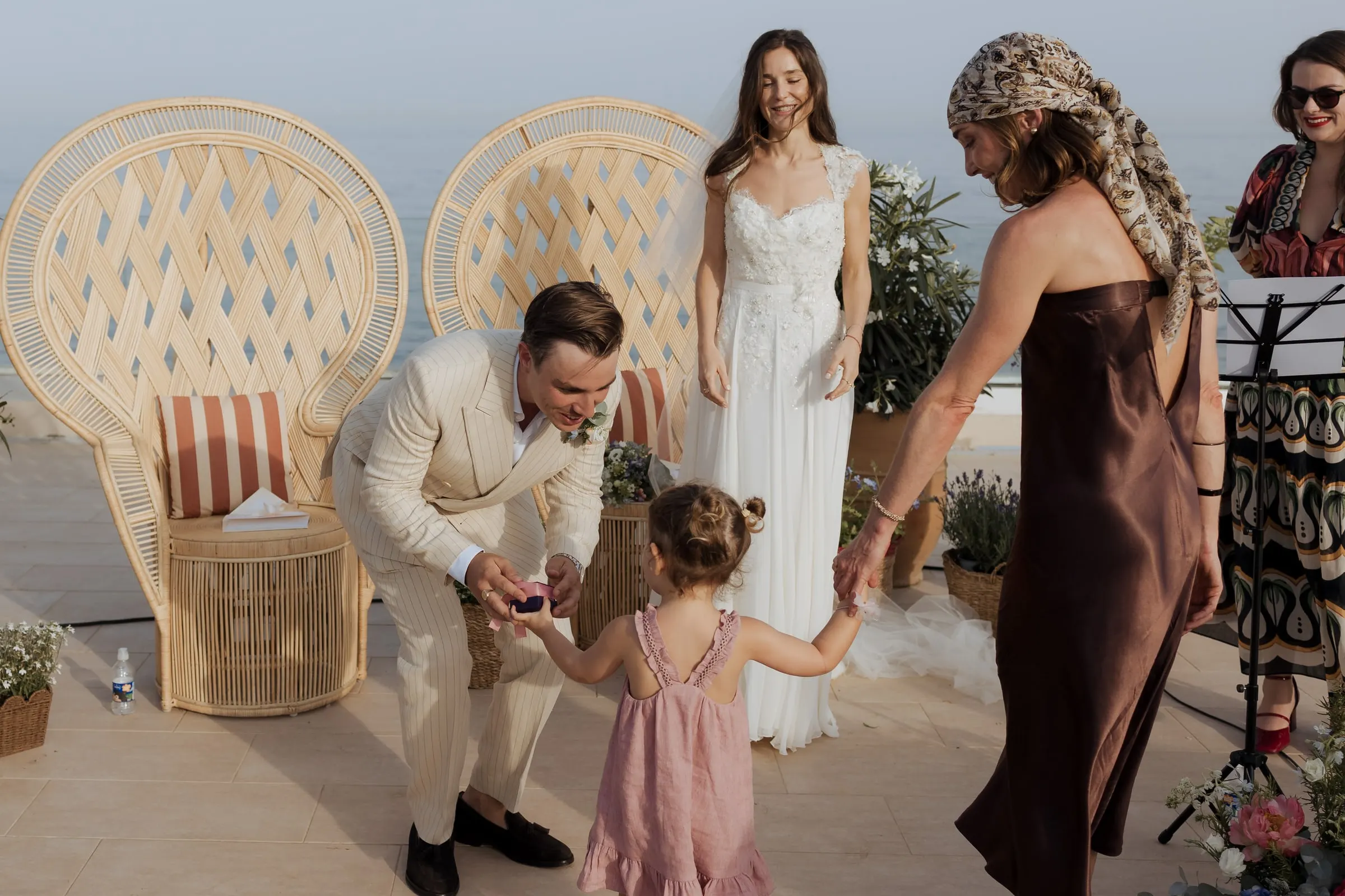 Groom bending to take the rings from a little girl in pink as the bride smiles, ceremony at Barbillón, Marbella