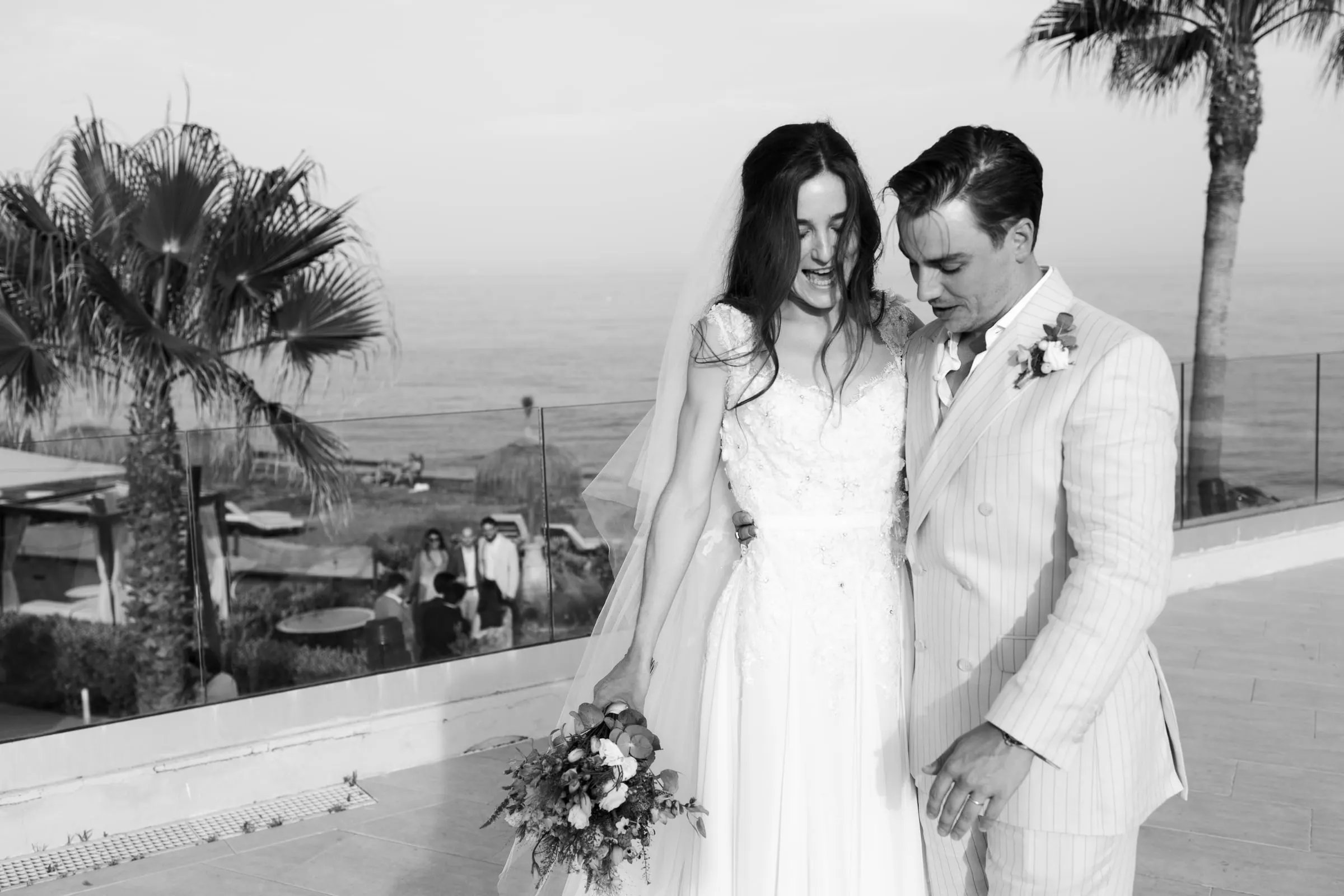 Black and white of the couple laughing on the terrace with palms and the sea, Barbillón, Marbella