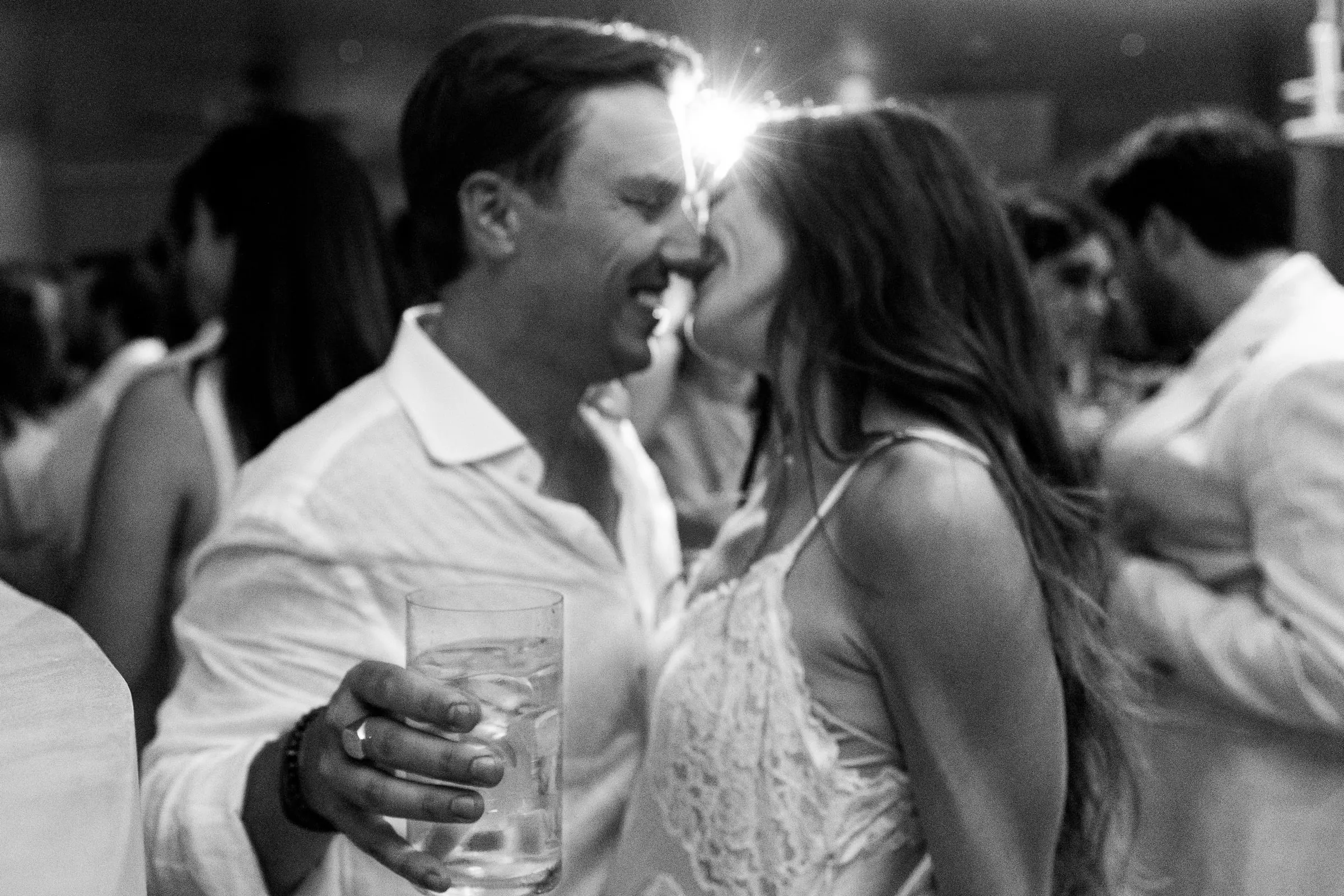 Black and white of the couple kissing among guests during the party, Barbillón, Marbella