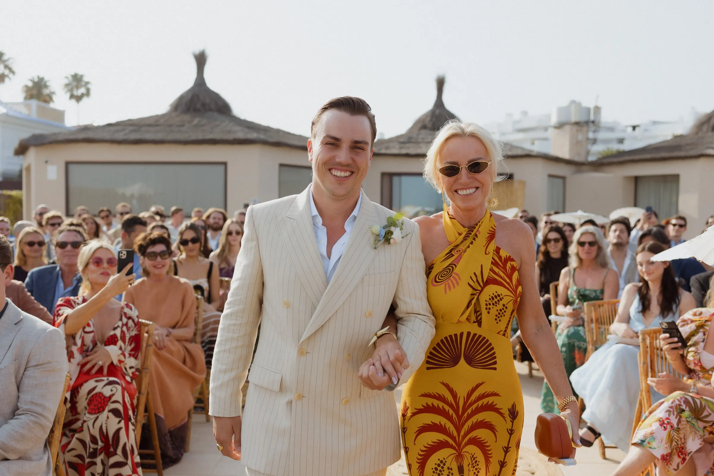 Groom walking down the aisle arm in arm with a woman in a yellow palm-print dress, Barbillón, Marbella