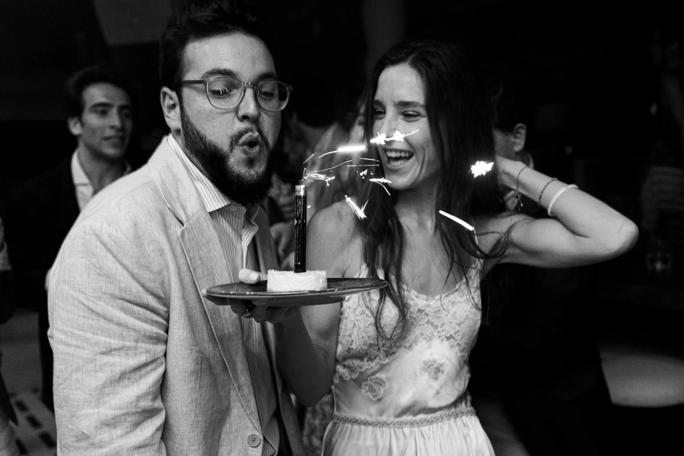 Black and white of the bride laughing beside a guest with a sparkler dessert, Barbillón, Marbella
