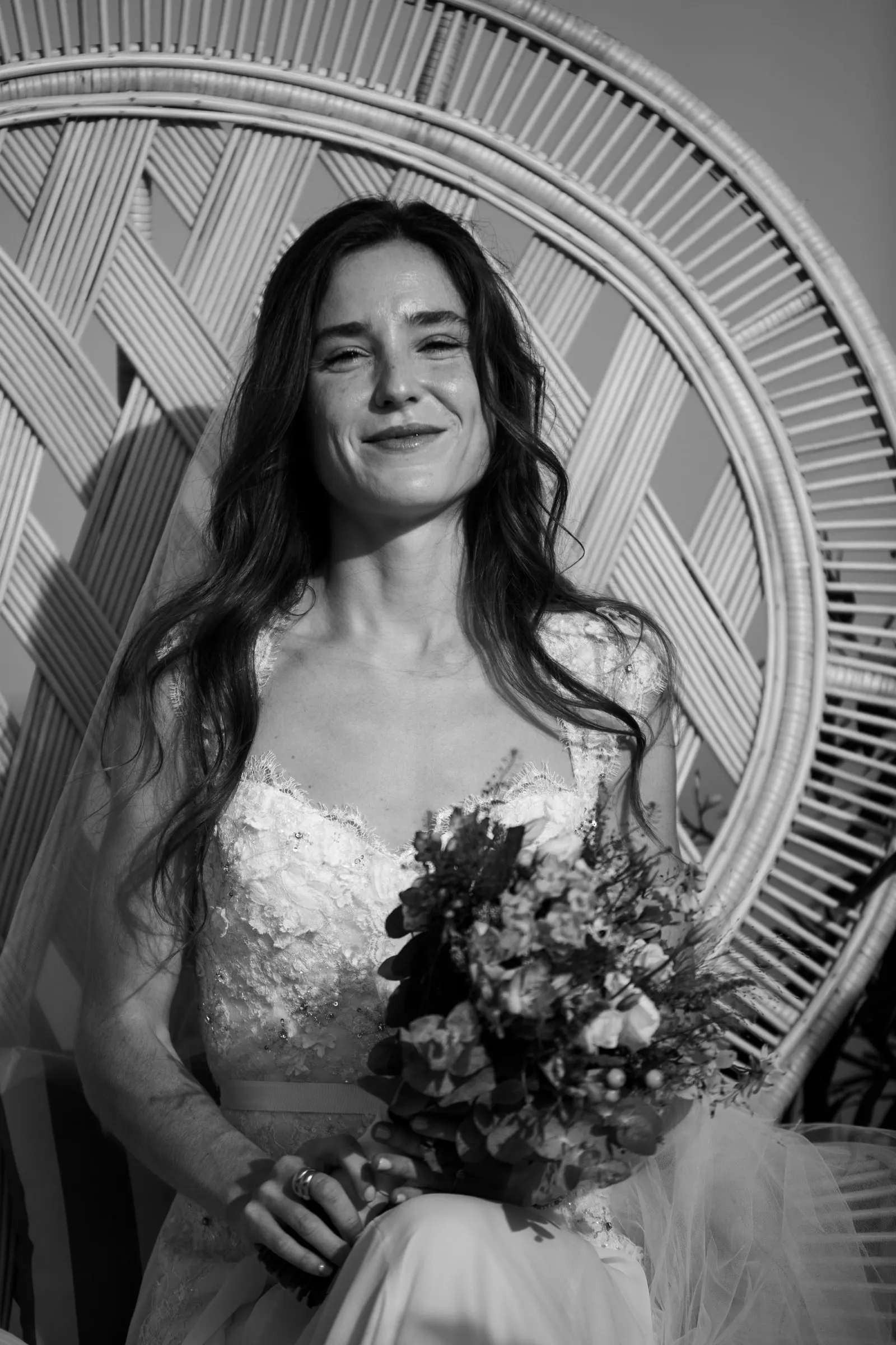 Black and white of the bride smiling in a wicker peacock chair with her bouquet, Barbillón, Marbella