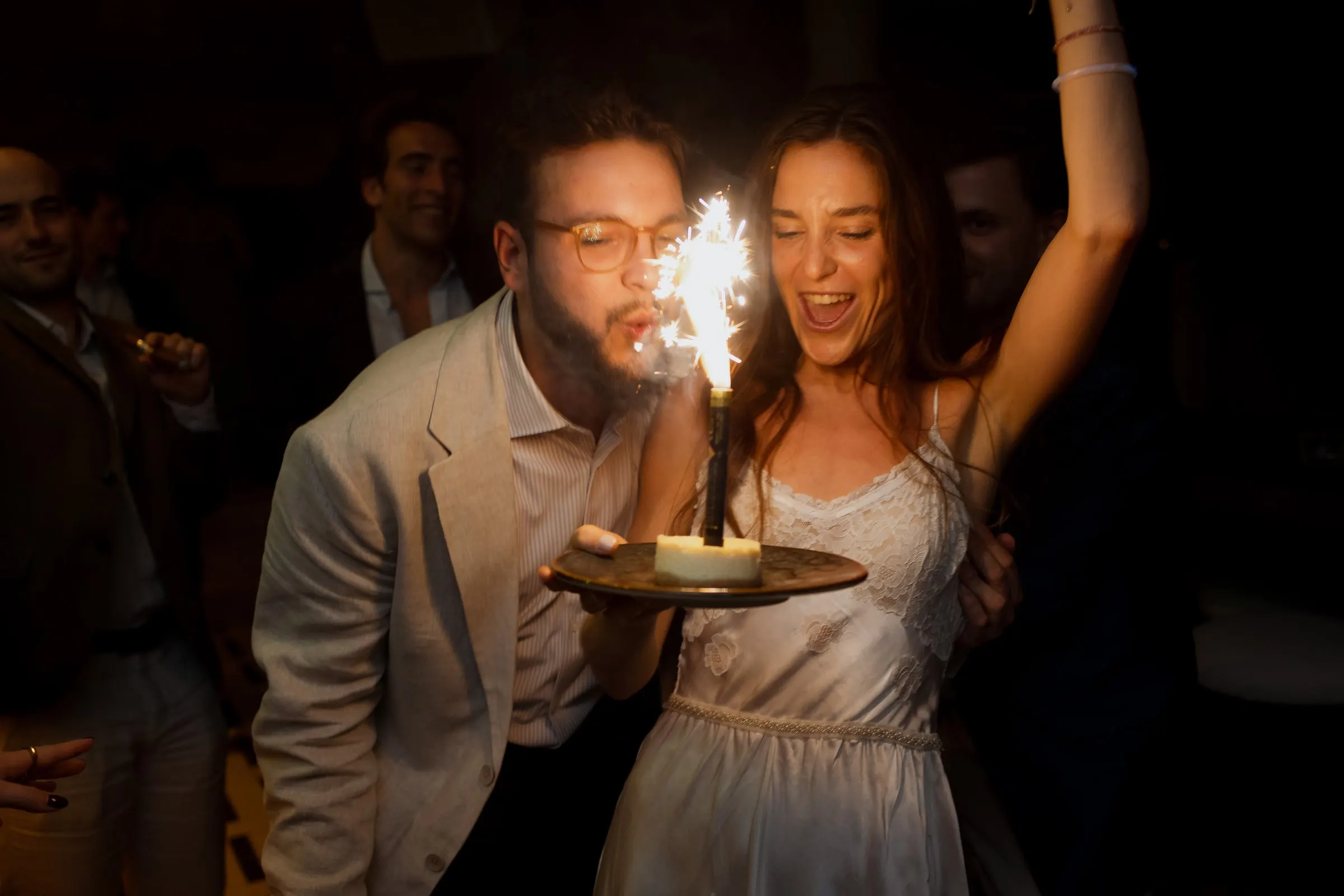 Bride laughing with an arm raised beside a guest with a sparkler at night, Barbillón, Marbella