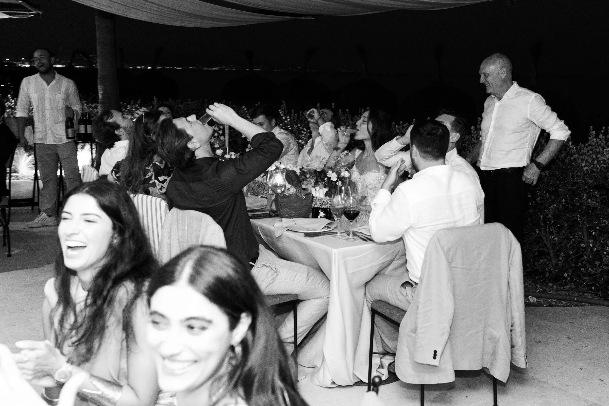 Black and white of the couple and guests downing shots together at dinner, Barbillón, Marbella