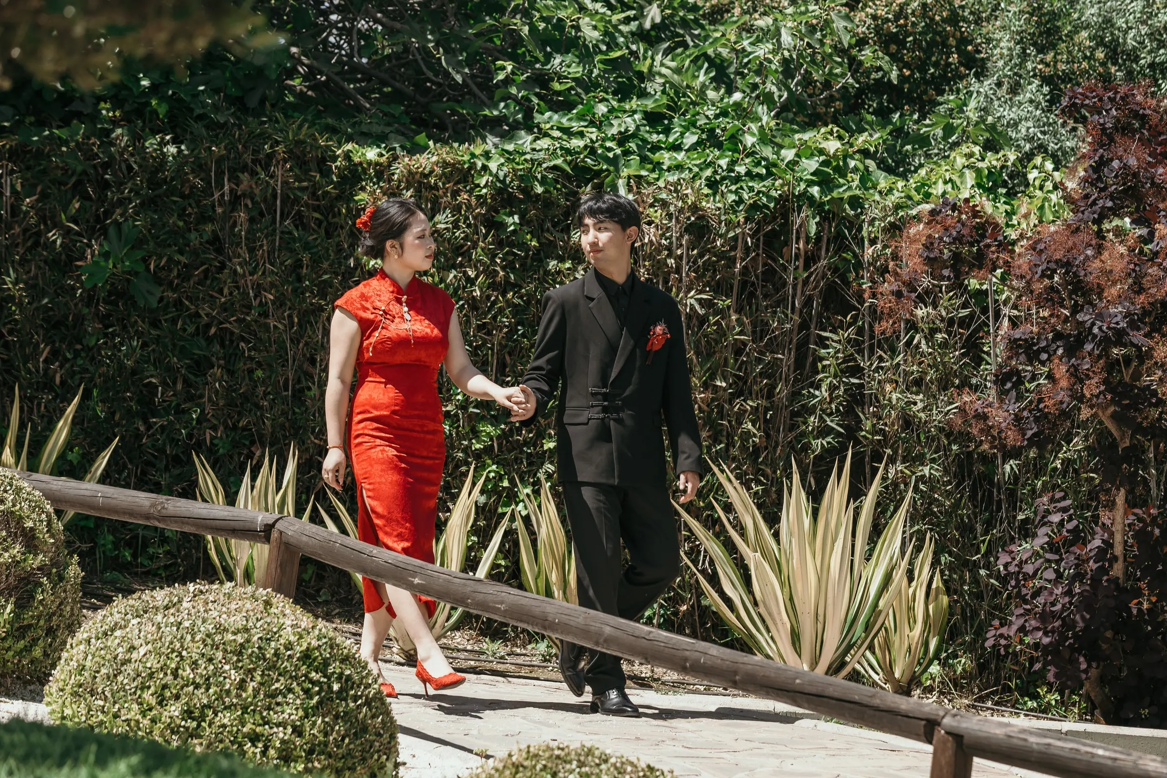 Couple walking hand in hand along a path lined with agaves and hedges, Jardín Oriental Bienquerido