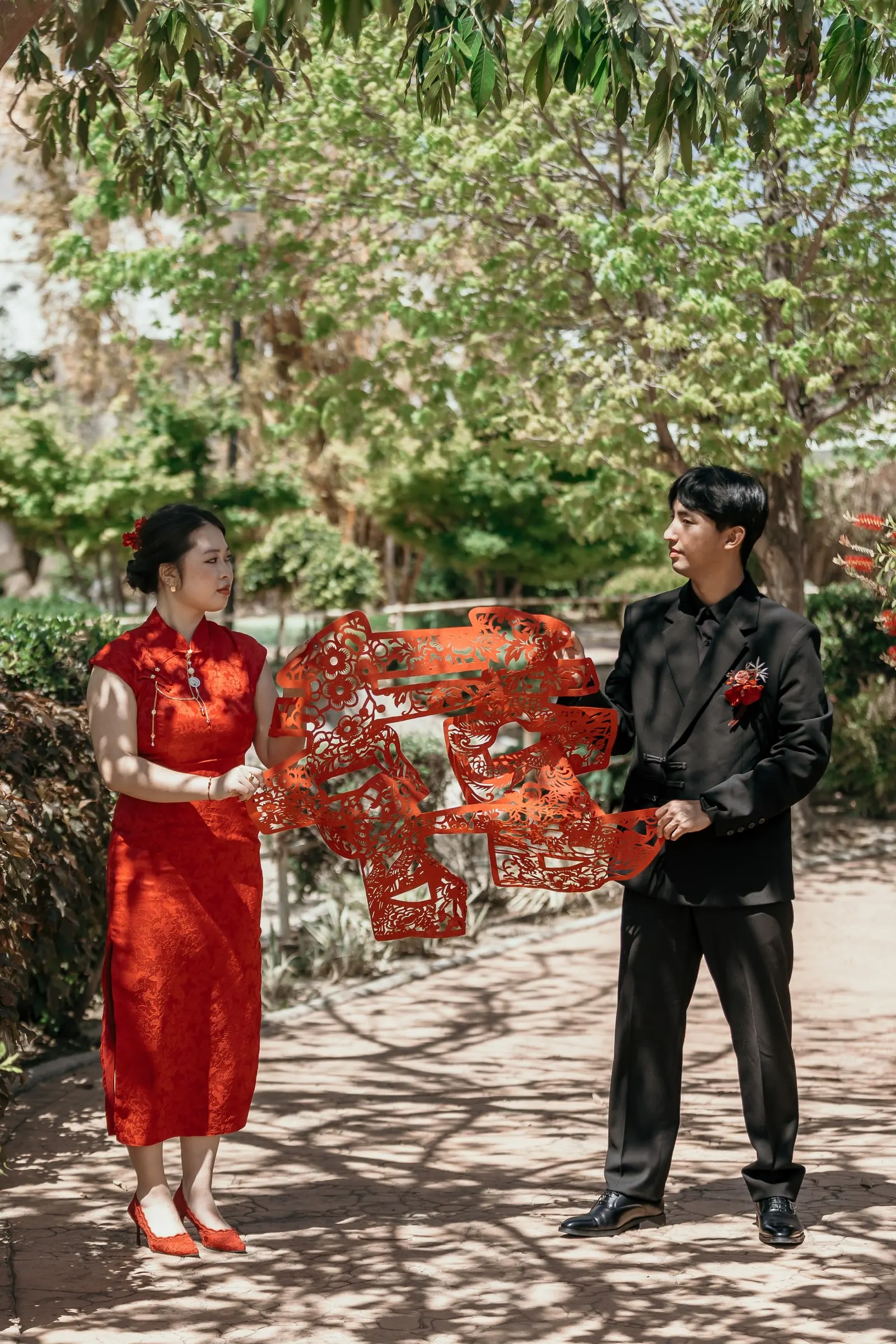 Couple holding the red double happiness paper-cut between them on a sunny garden path