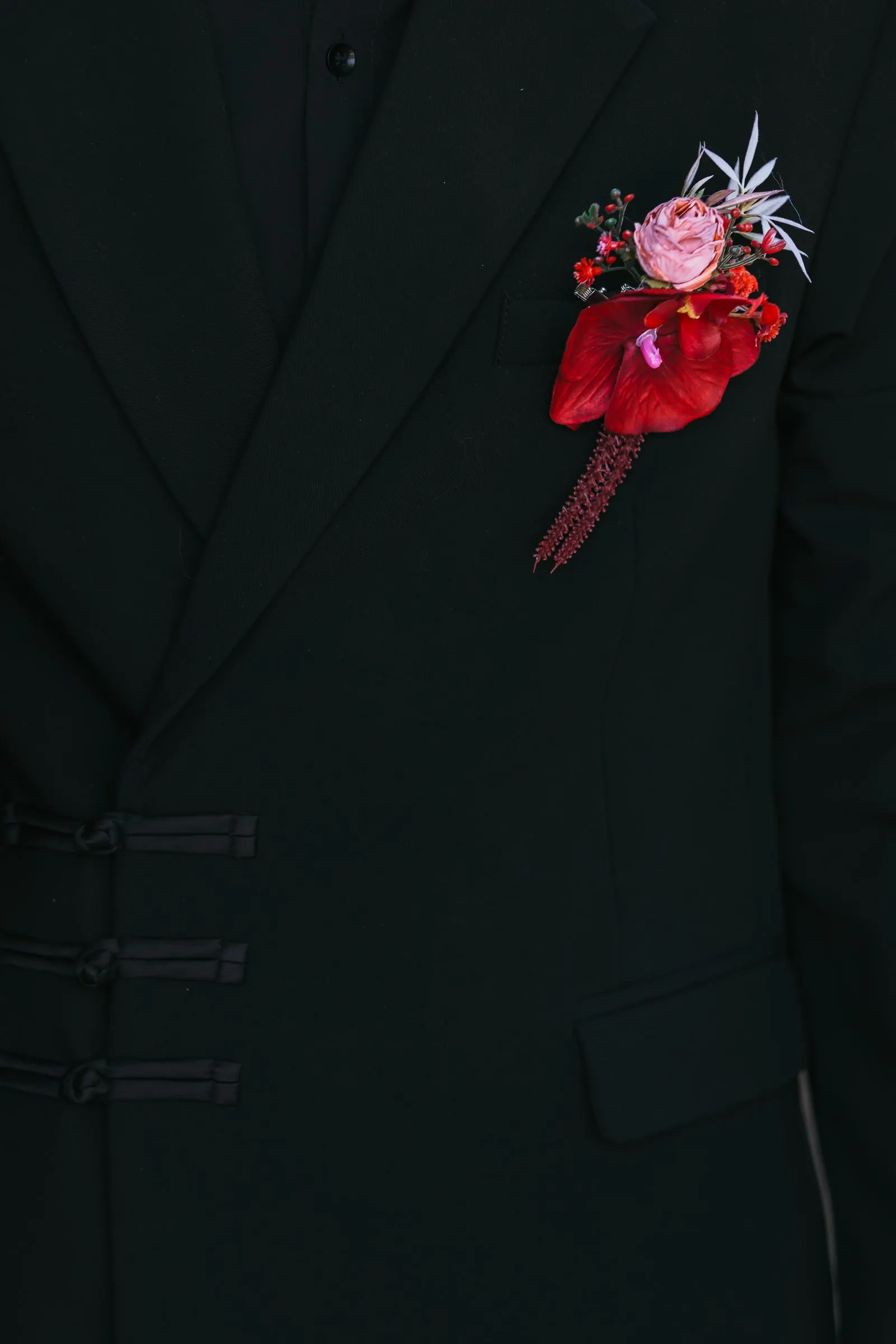 Red and pink flower boutonnière on a black jacket with frog buttons