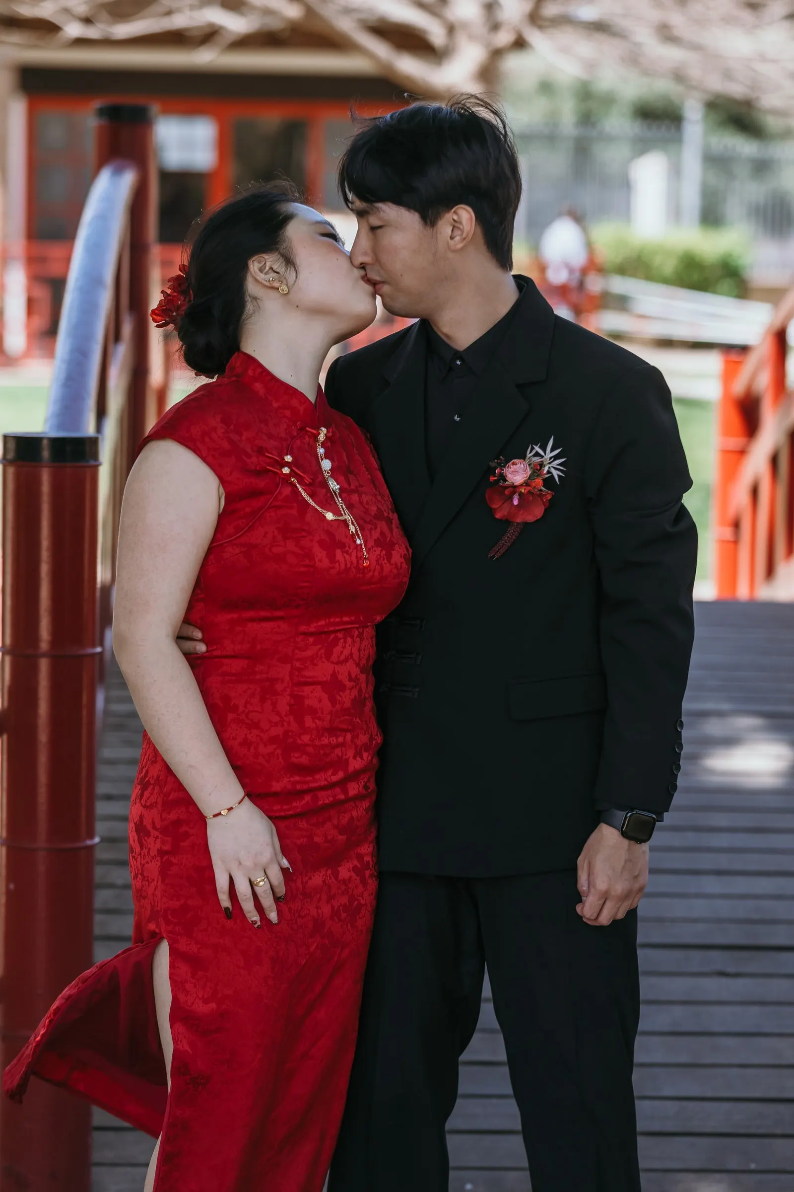 Couple kissing on a wooden bridge with red railings in the Jardín Oriental Bienquerido
