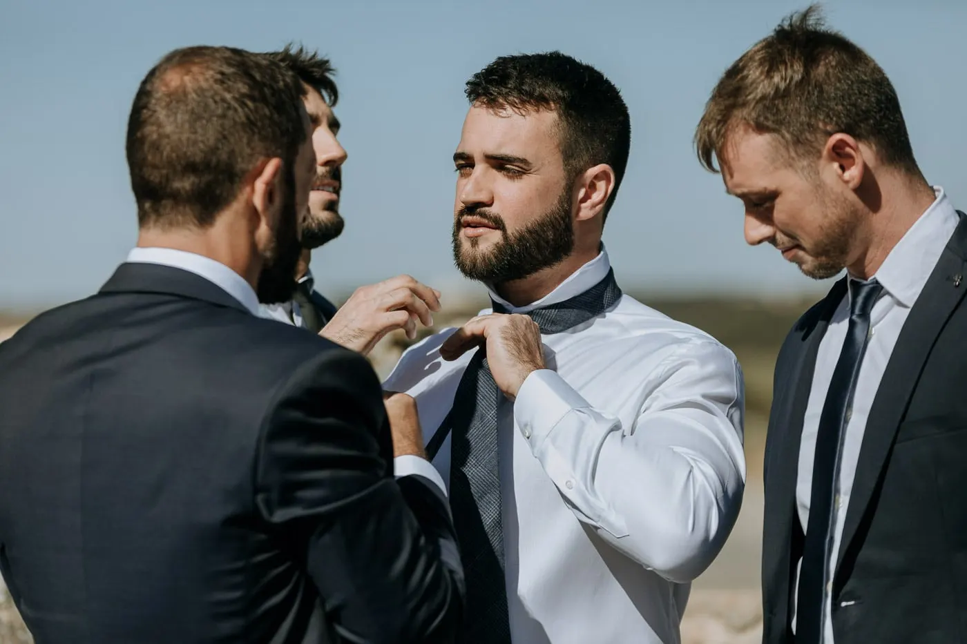 Friends in dark suits helping the groom with his tie, Castillo del Buen Amor
