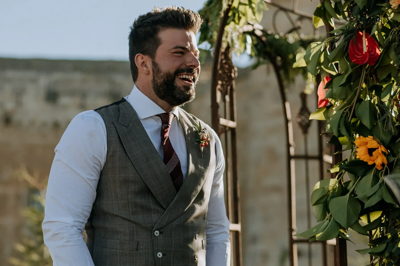 Groom laughing beside the arch of sunflowers and red flowers, Salamanca