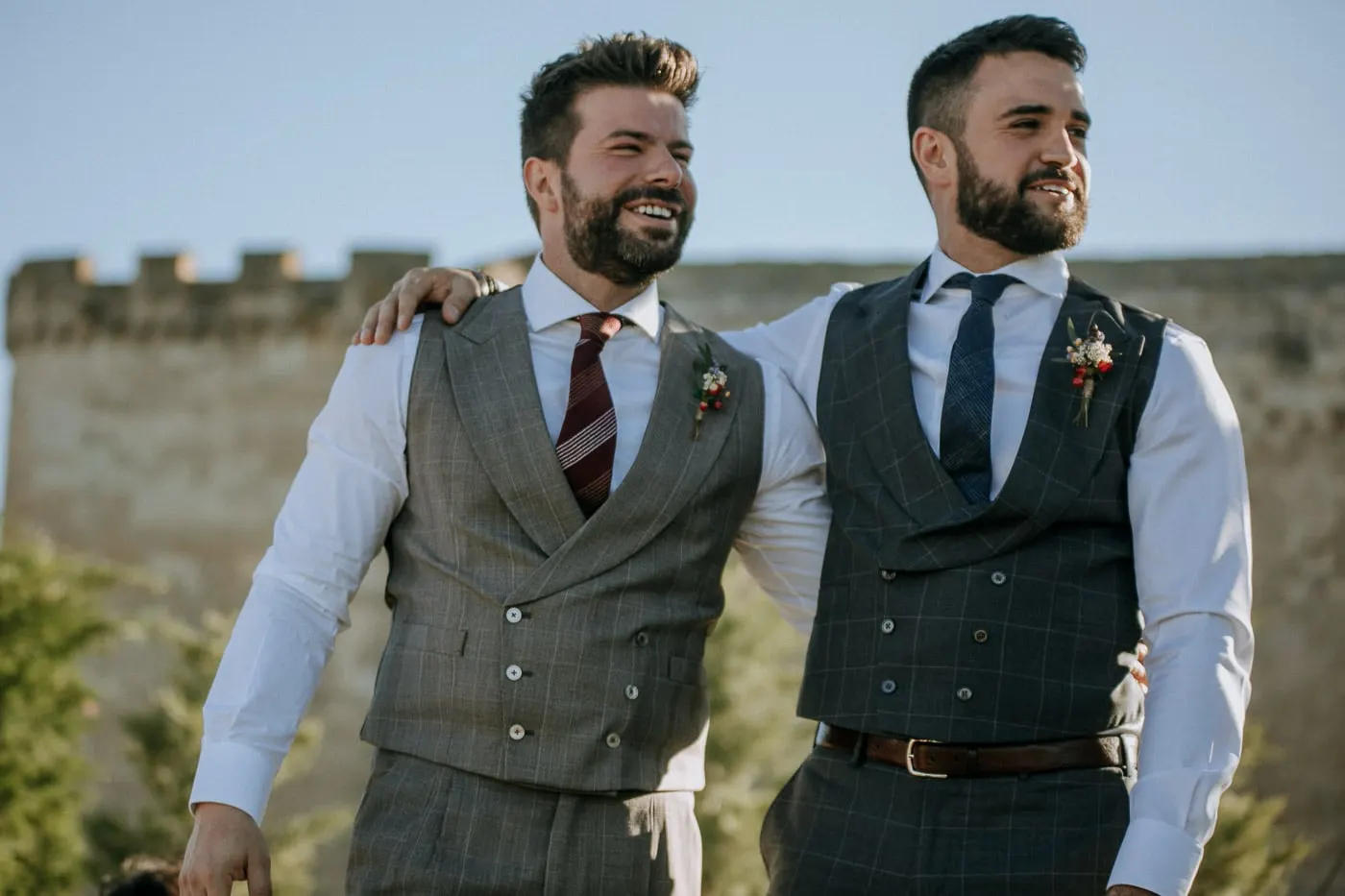 The two grooms arm in arm, smiling, in front of the battlements, Salamanca