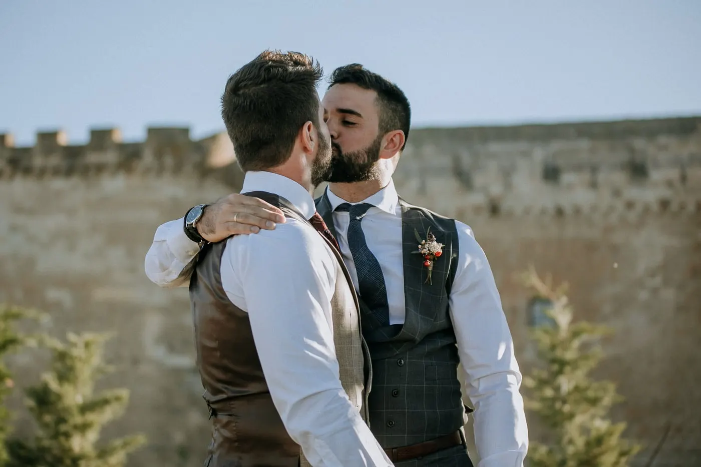 The grooms kissing after the ceremony in front of the castle walls, Castillo del Buen Amor