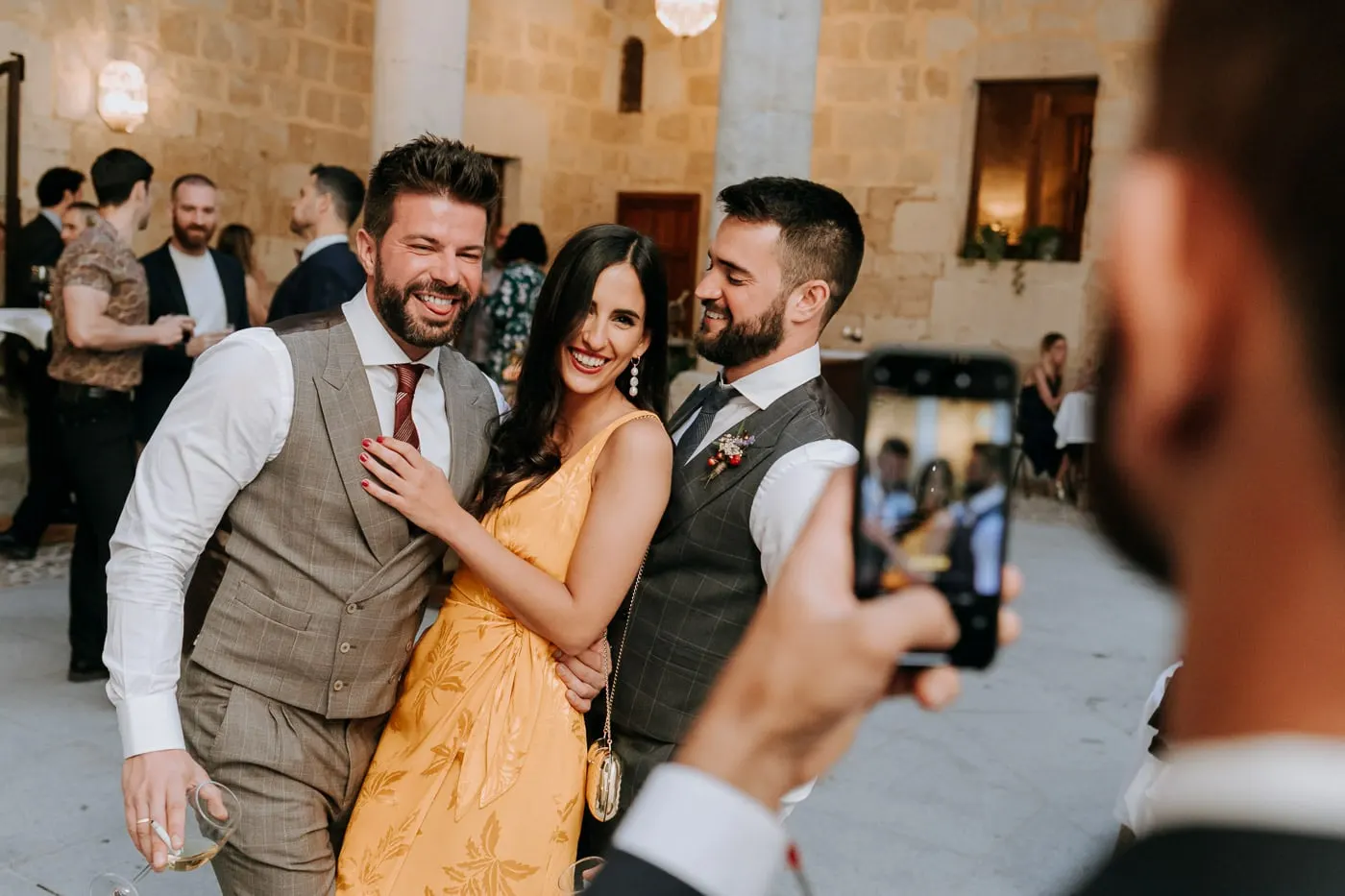 The grooms posing with a friend for a phone photo in the courtyard, Castillo del Buen Amor
