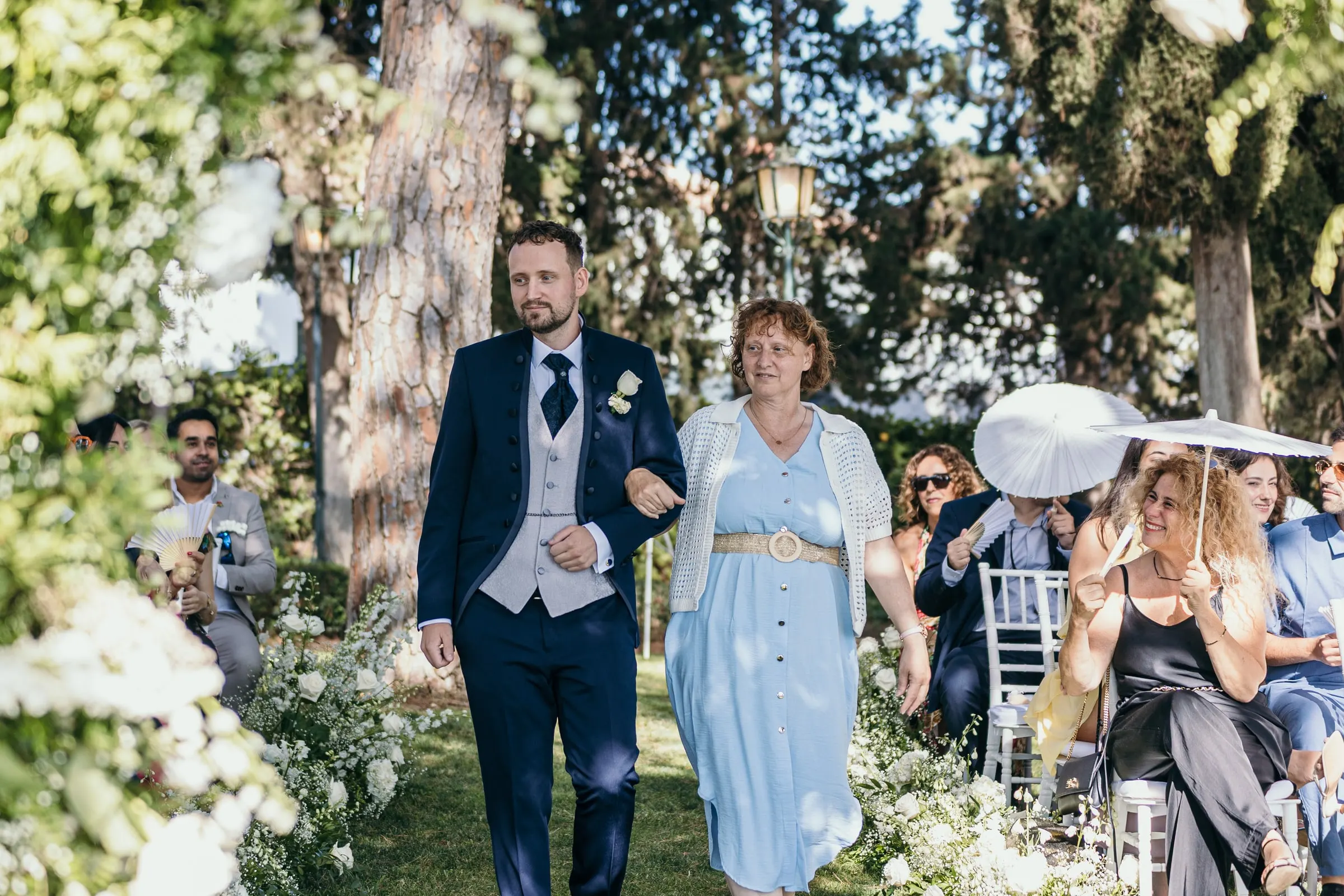 Vincent walks down the garden aisle with a woman in a pale blue dress as guests watch from their seats