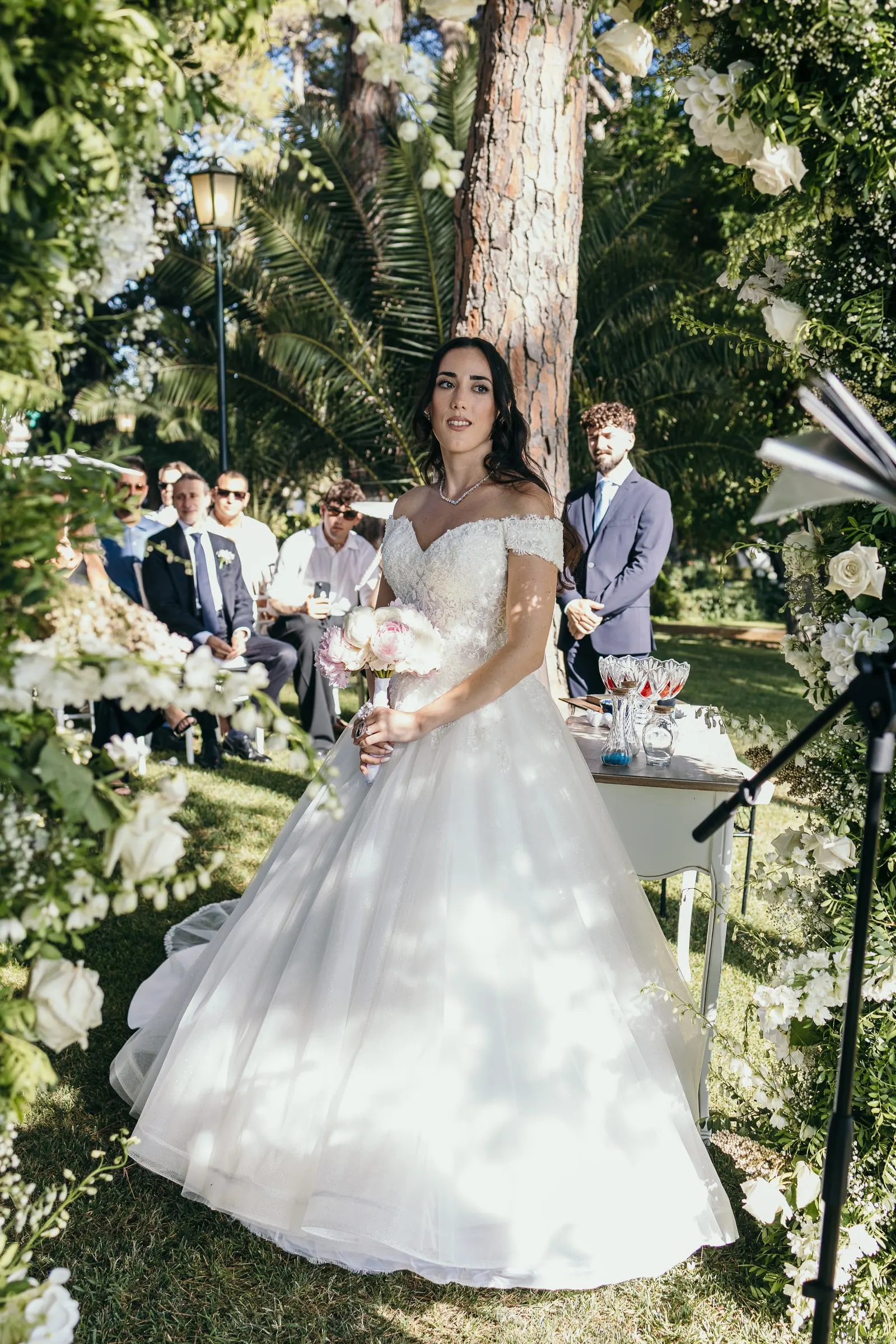 Sara in her ball gown at the ceremony table, surrounded by greenery and white blooms