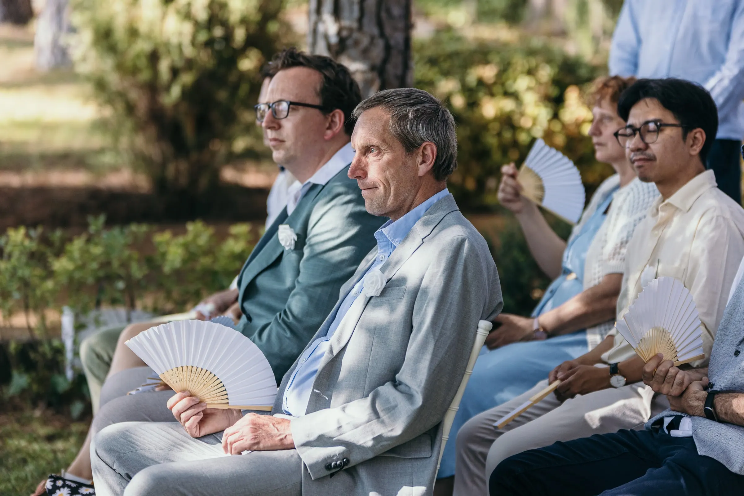 Guests with white paper fans listen to the ceremony in the hotel garden