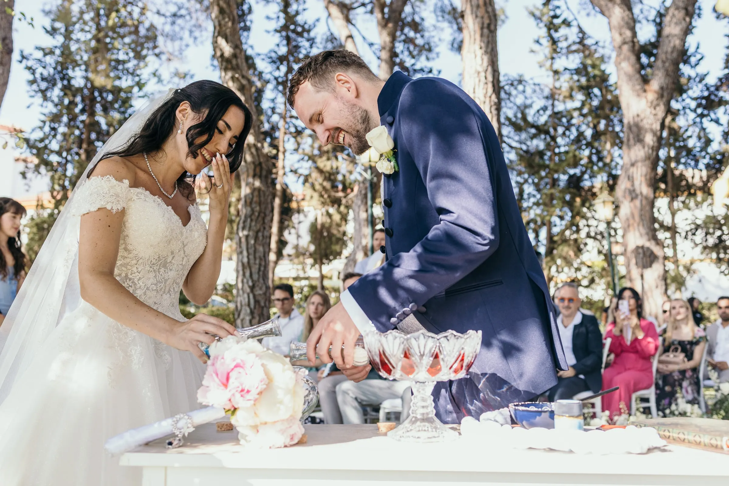 Sara and Vincent pour coloured sand together at the ceremony table under the pines