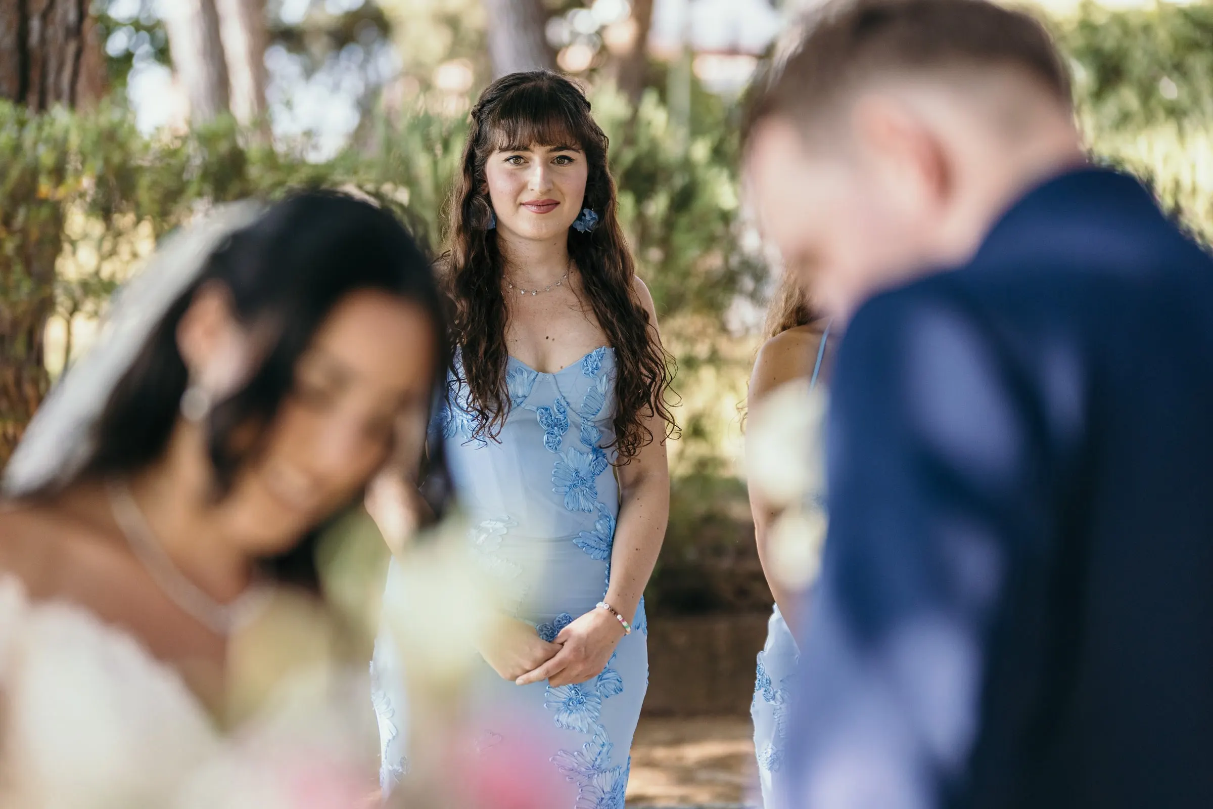 A bridesmaid in blue watches the couple during the ceremony