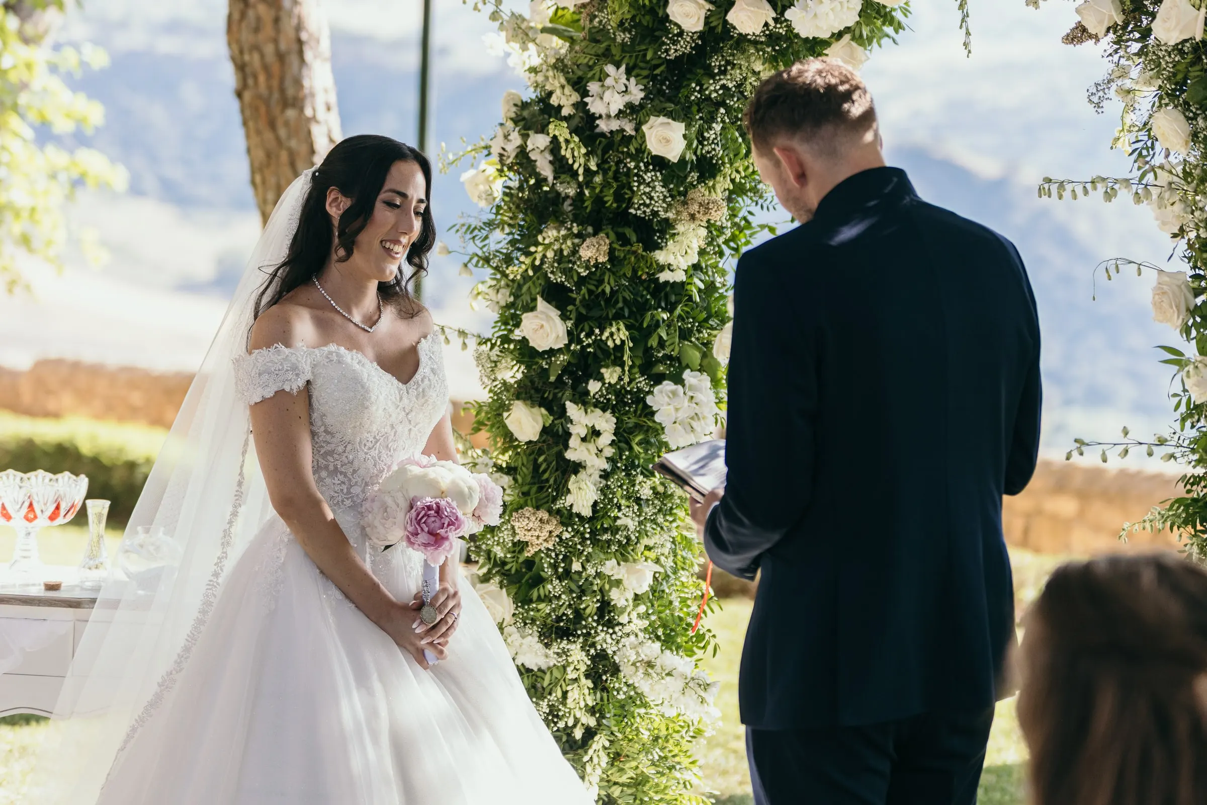 Sara listens as Vincent reads beside the arch of white roses