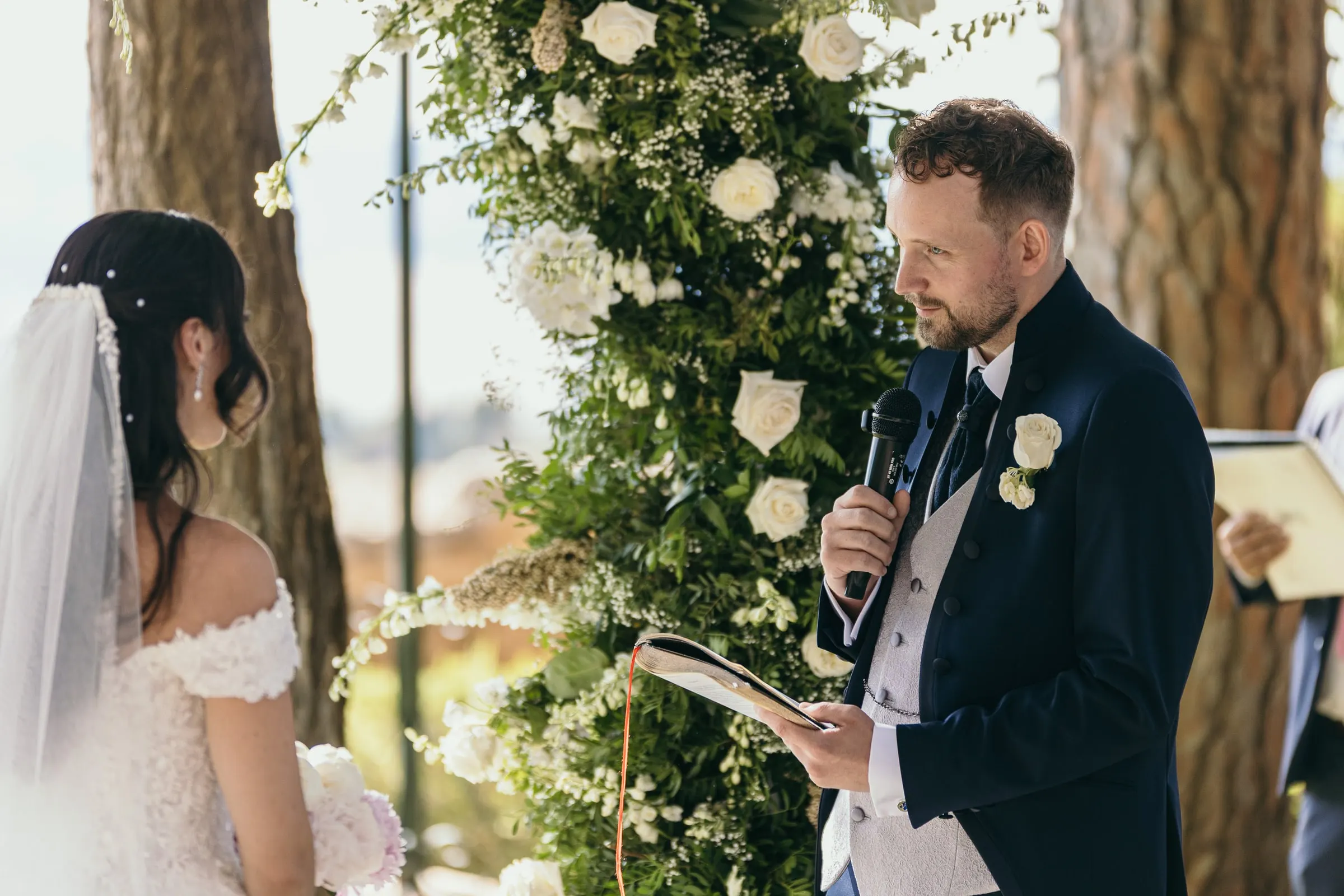 Vincent reads his vows into a microphone in front of the white rose arch