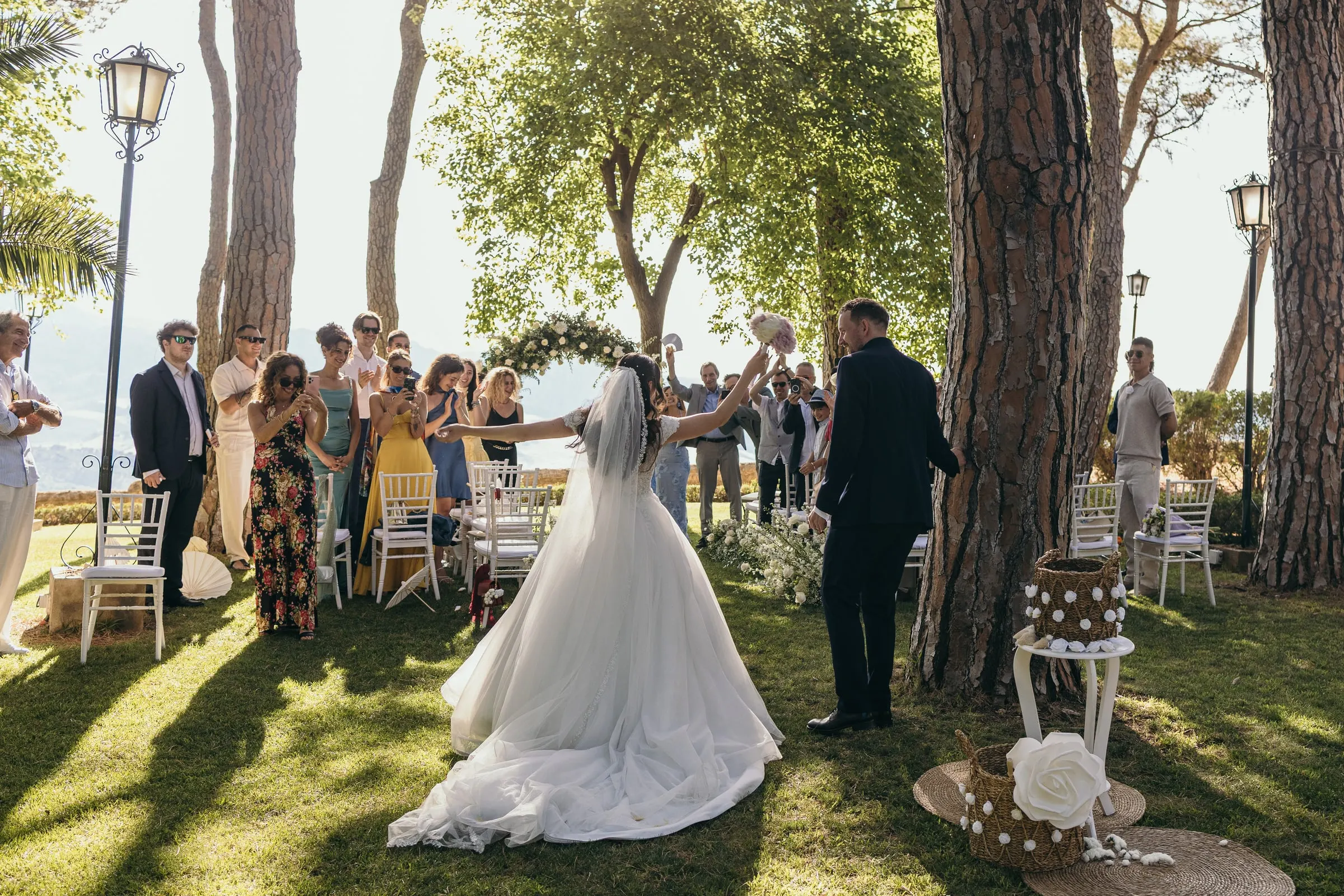 Sara's long veil trails over the grass as guests applaud the newlyweds