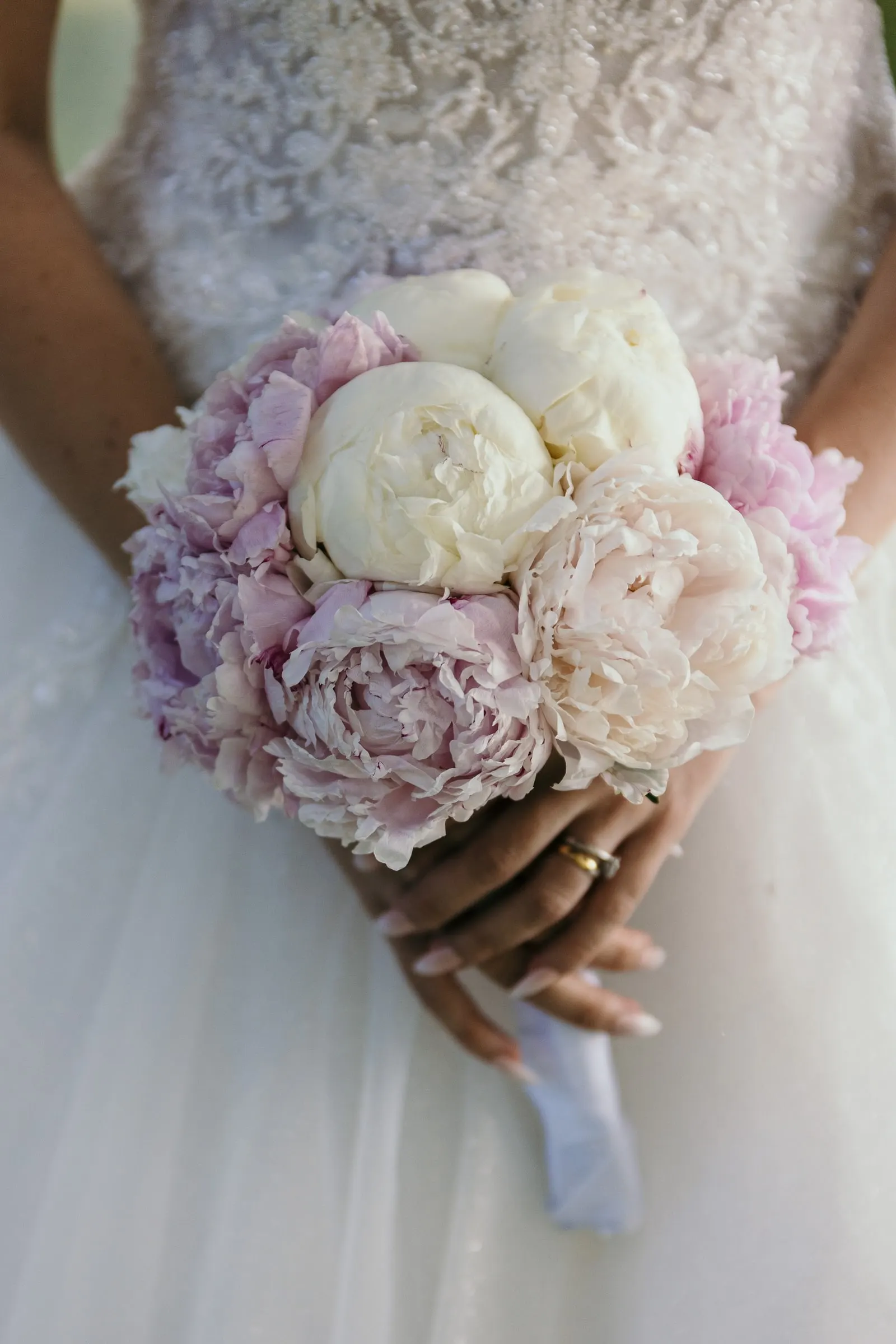 Close-up of Sara's bouquet of white and pink peonies against her lace dress