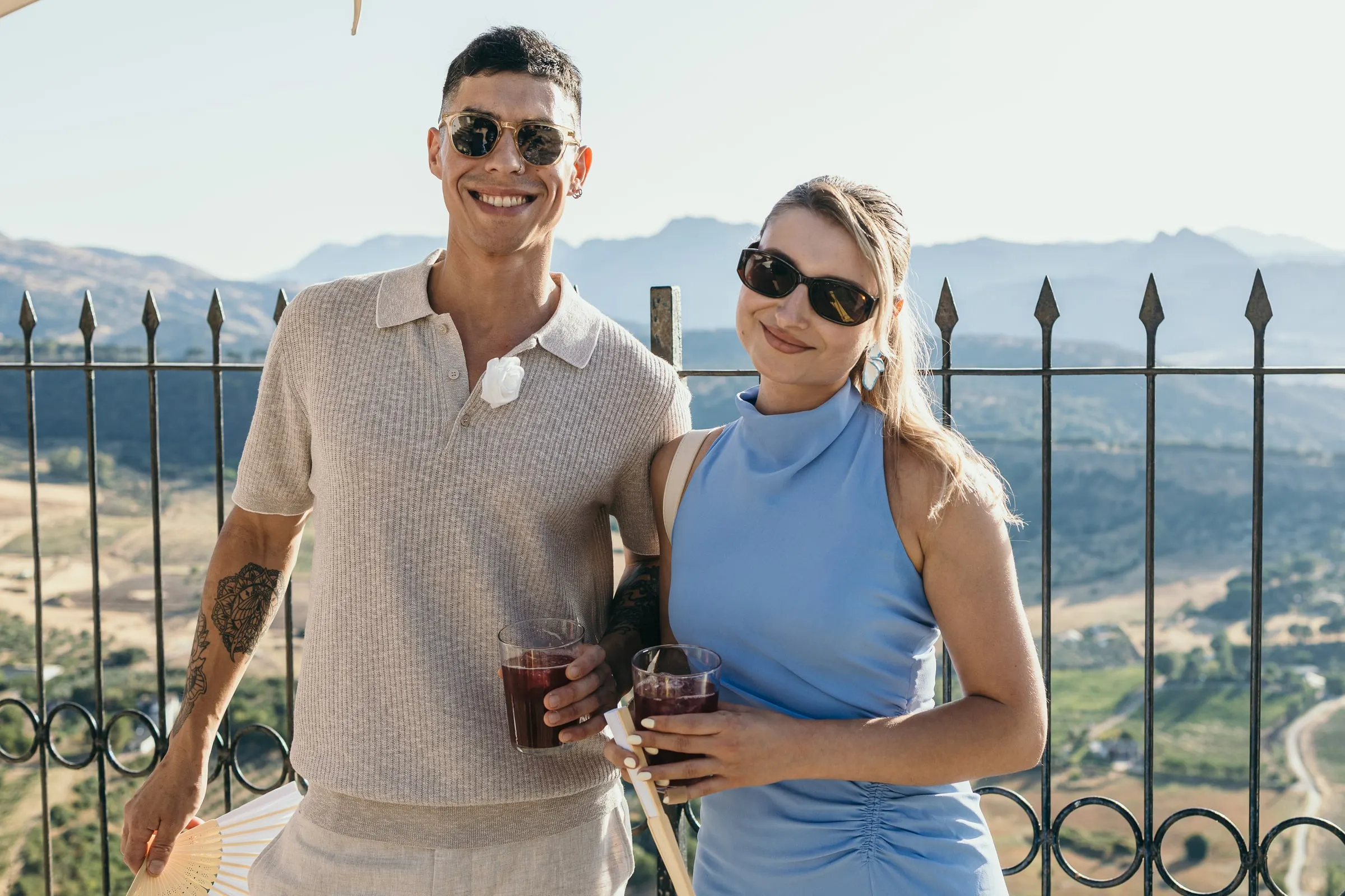 Two guests with drinks by the iron railing over the valley at sunset