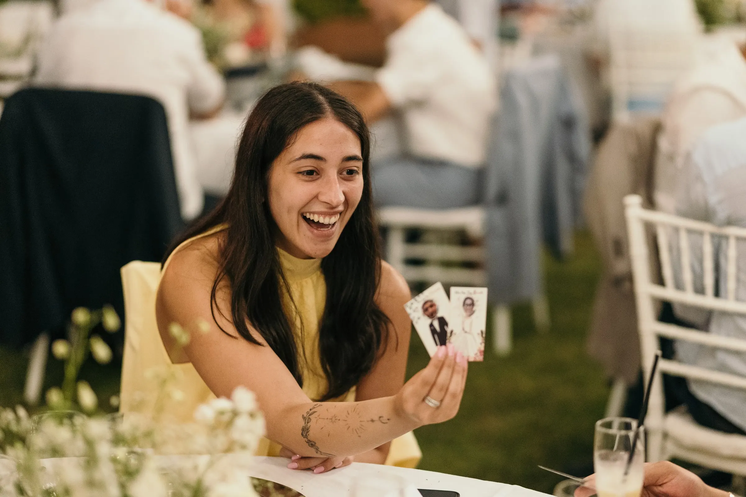 A guest laughs as she holds up a photo card at dinner