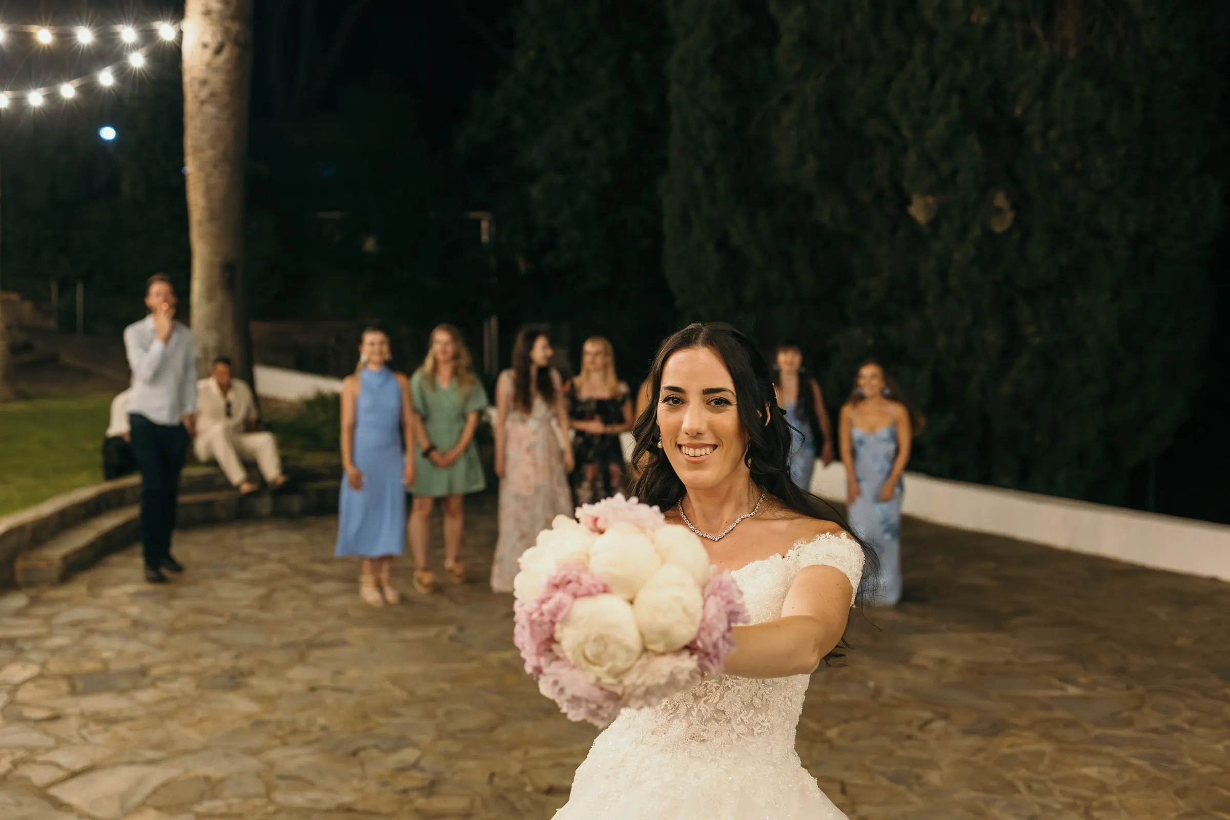Sara gets ready to throw her bouquet on the stone patio at night