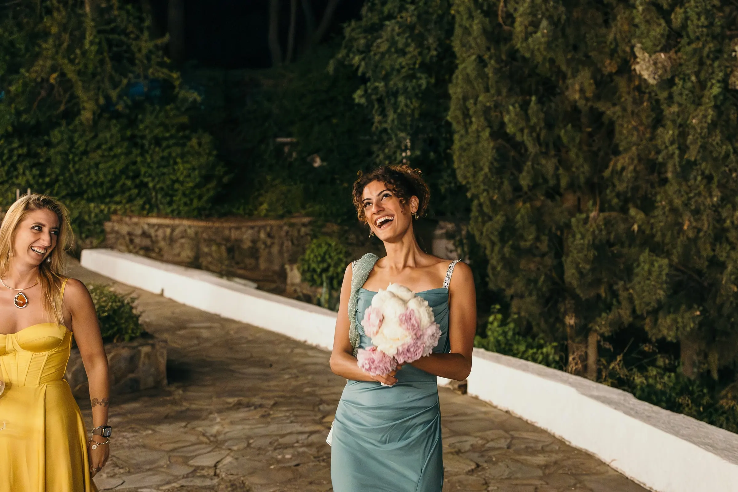 A guest laughs after catching the bouquet on the garden path