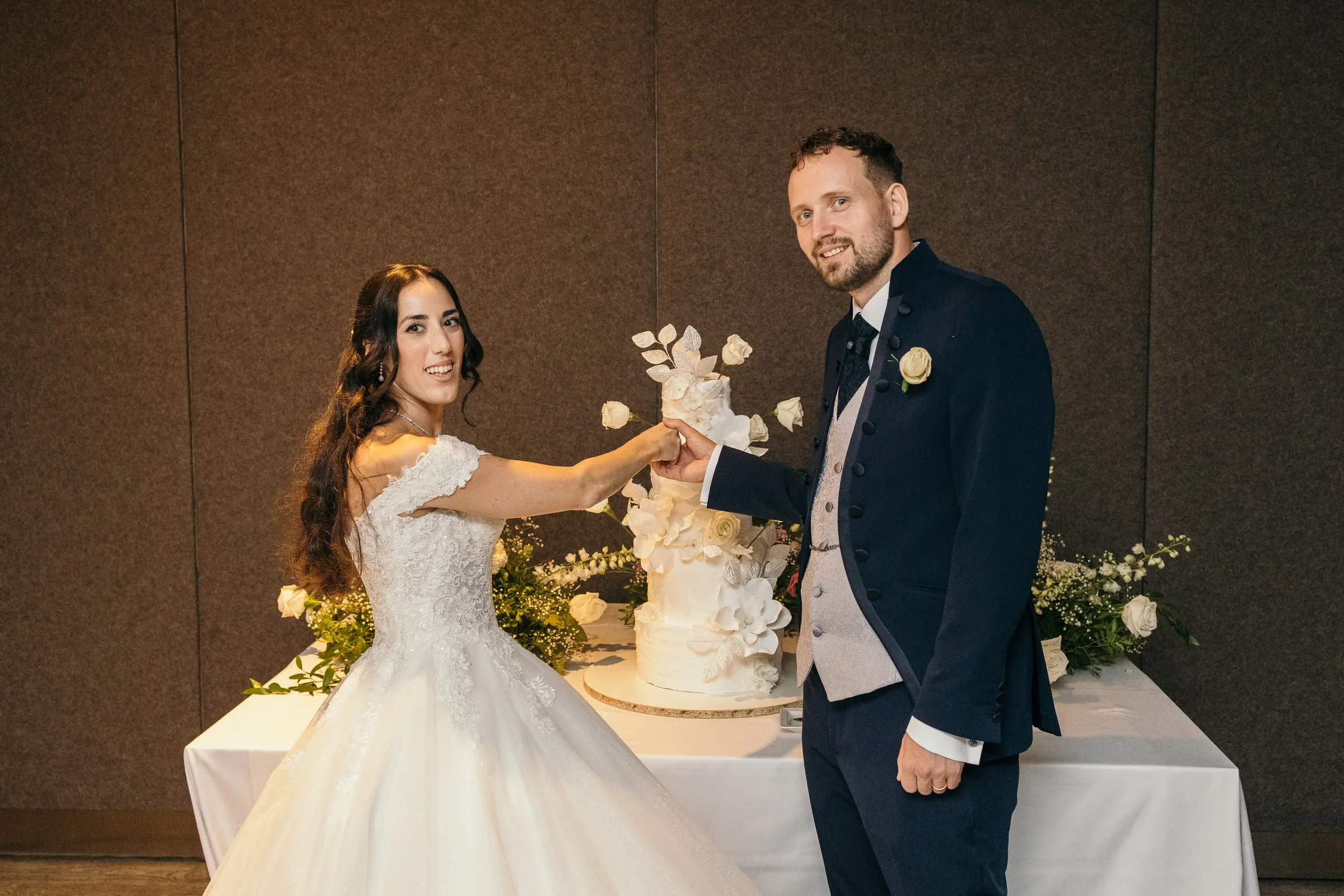 Sara and Vincent cut their white wedding cake decorated with flowers