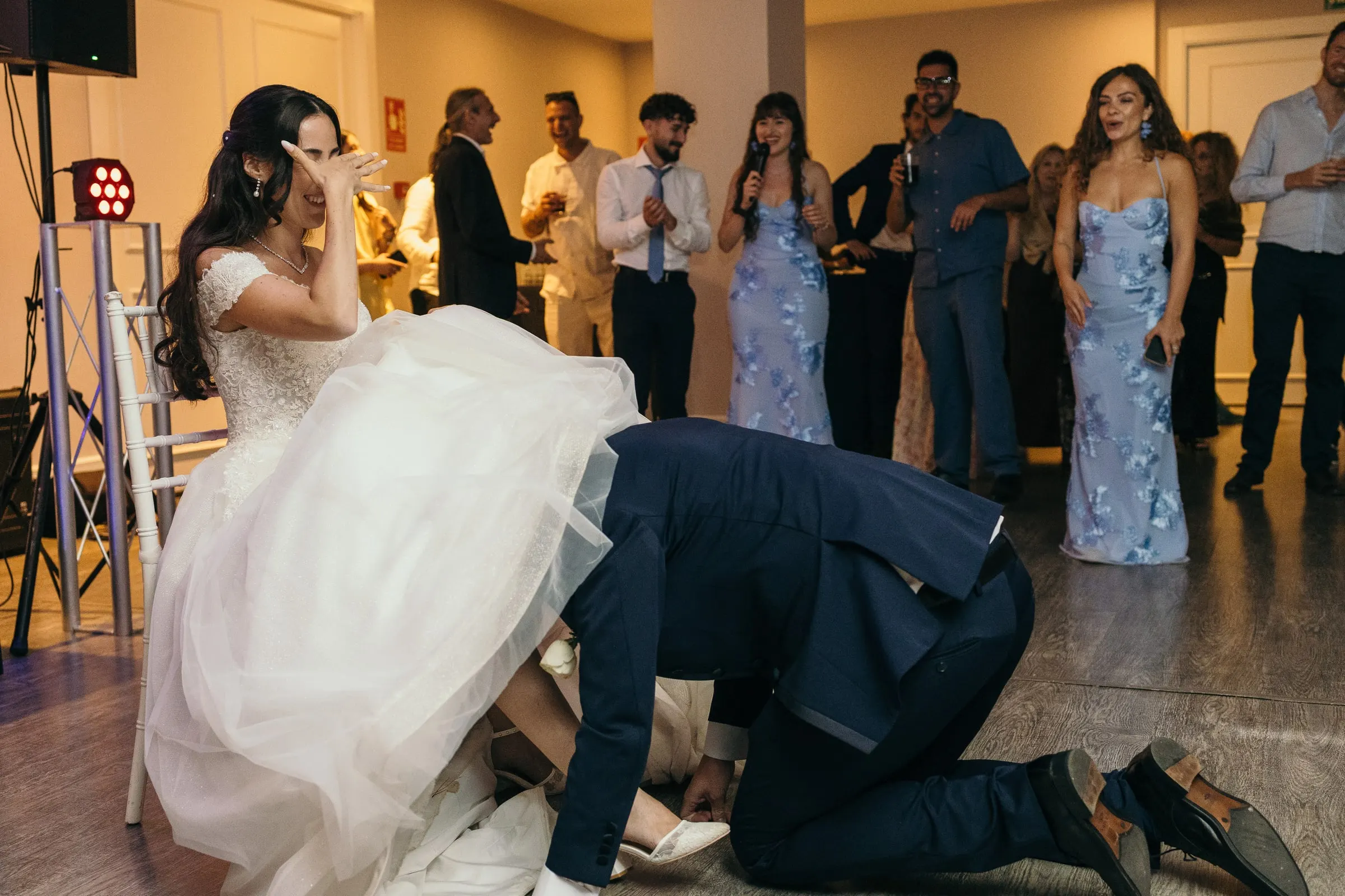 Vincent kneels under Sara's skirt for the garter as guests watch
