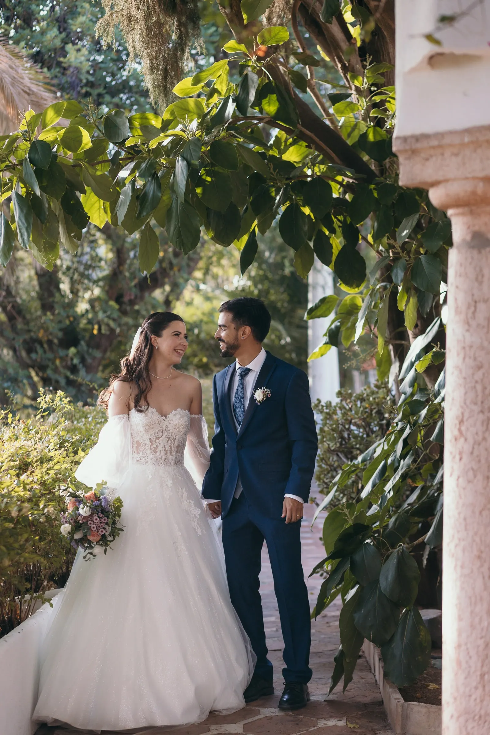 Bride and groom holding hands under a garden arcade full of plants, Cortijo San Francisco, Estepona