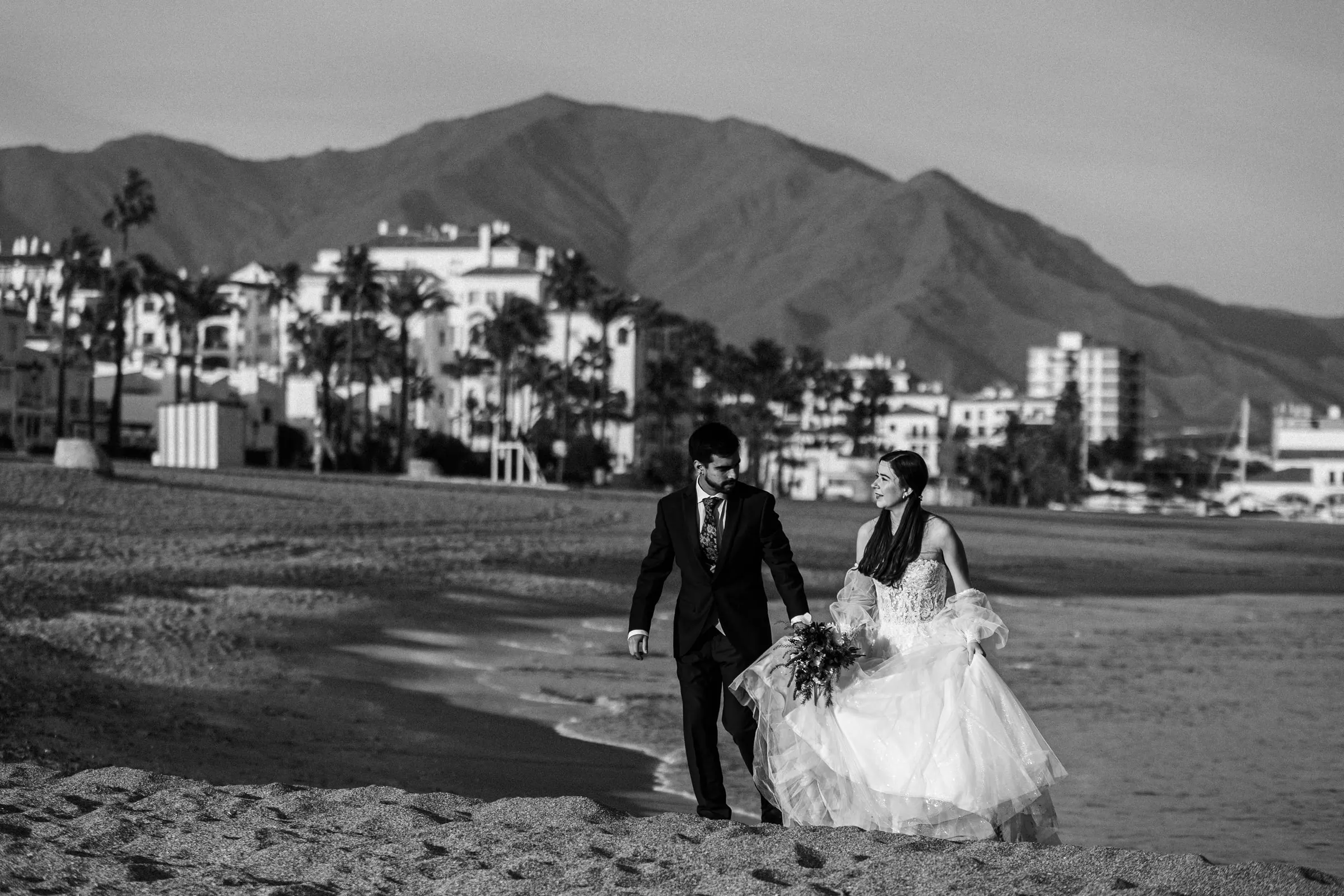 Black and white of the couple walking along the shore with the mountains behind, Cortijo San Francisco, Estepona