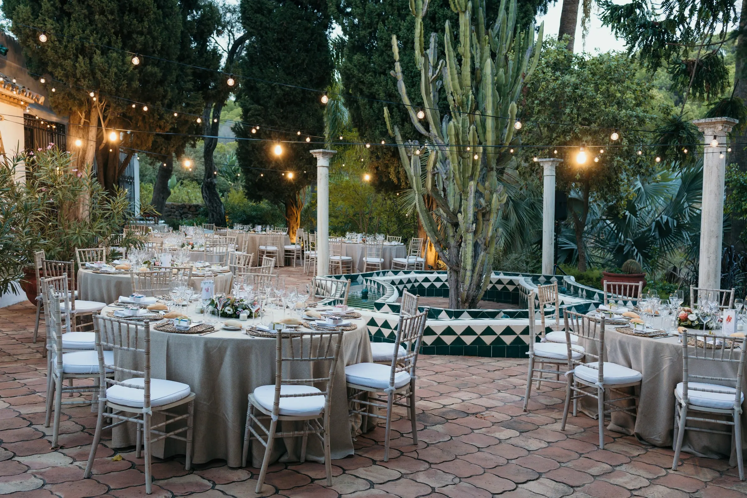 Banquet tables in the tiled courtyard under string lights and tall cacti, Cortijo San Francisco, Estepona