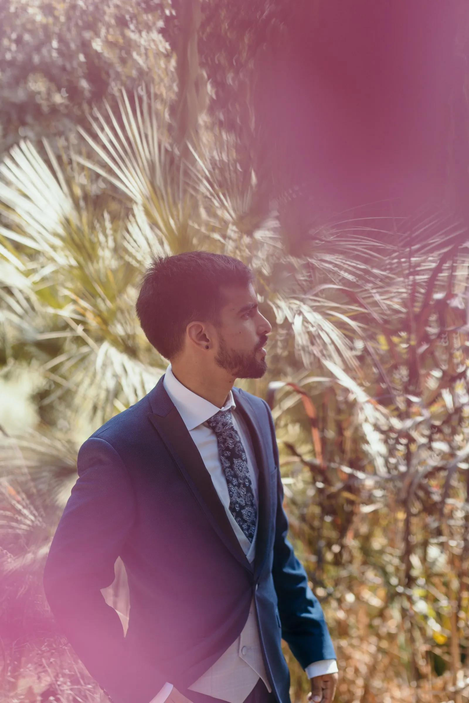 Groom in a navy suit and paisley tie among palm leaves in the garden, Cortijo San Francisco, Estepona