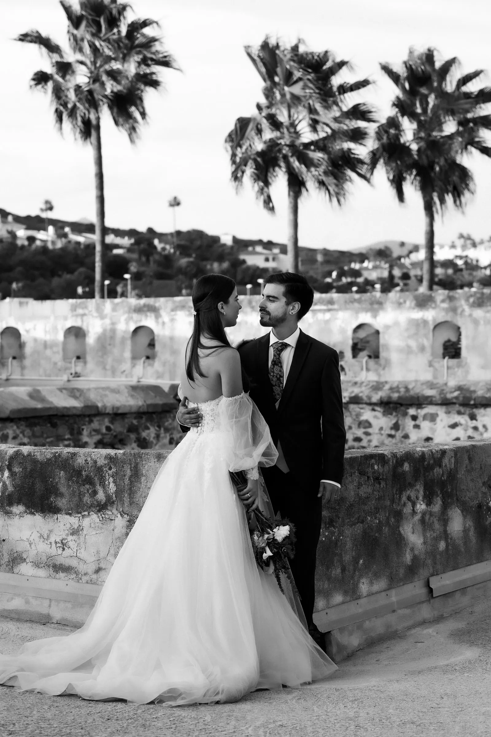 Black and white of the couple face to face on a terrace lined with palm trees, Cortijo San Francisco, Estepona