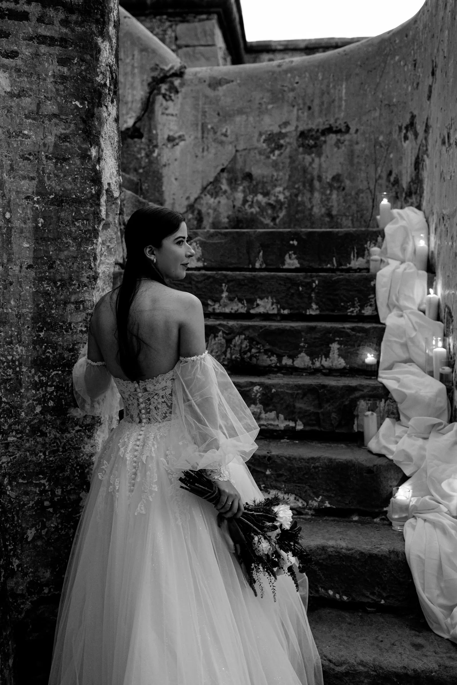 Black and white of the bride at the foot of worn stone steps with candles, Cortijo San Francisco, Estepona