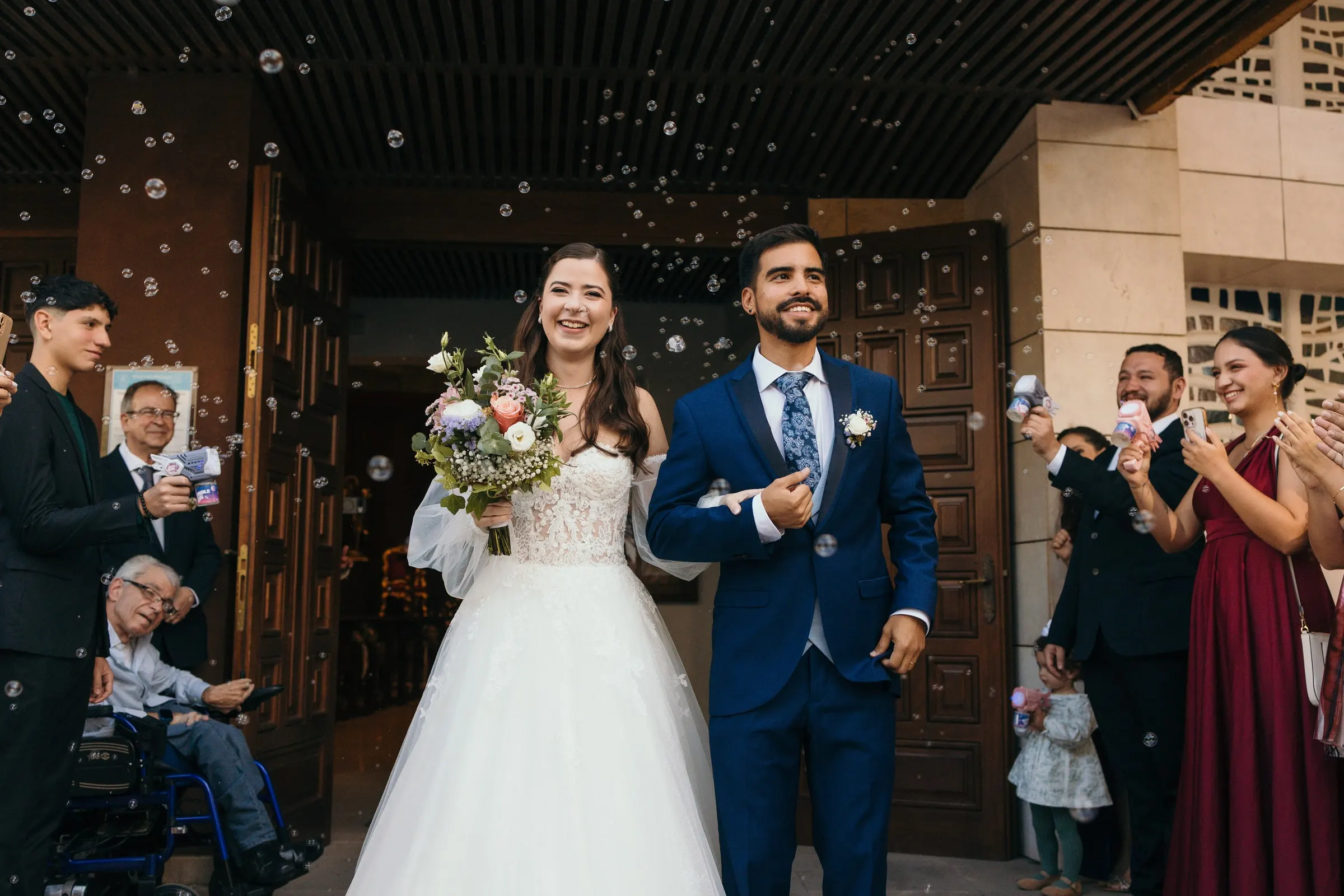 Couple leaving through a wooden door as guests cheer and blow bubbles, Cortijo San Francisco, Estepona