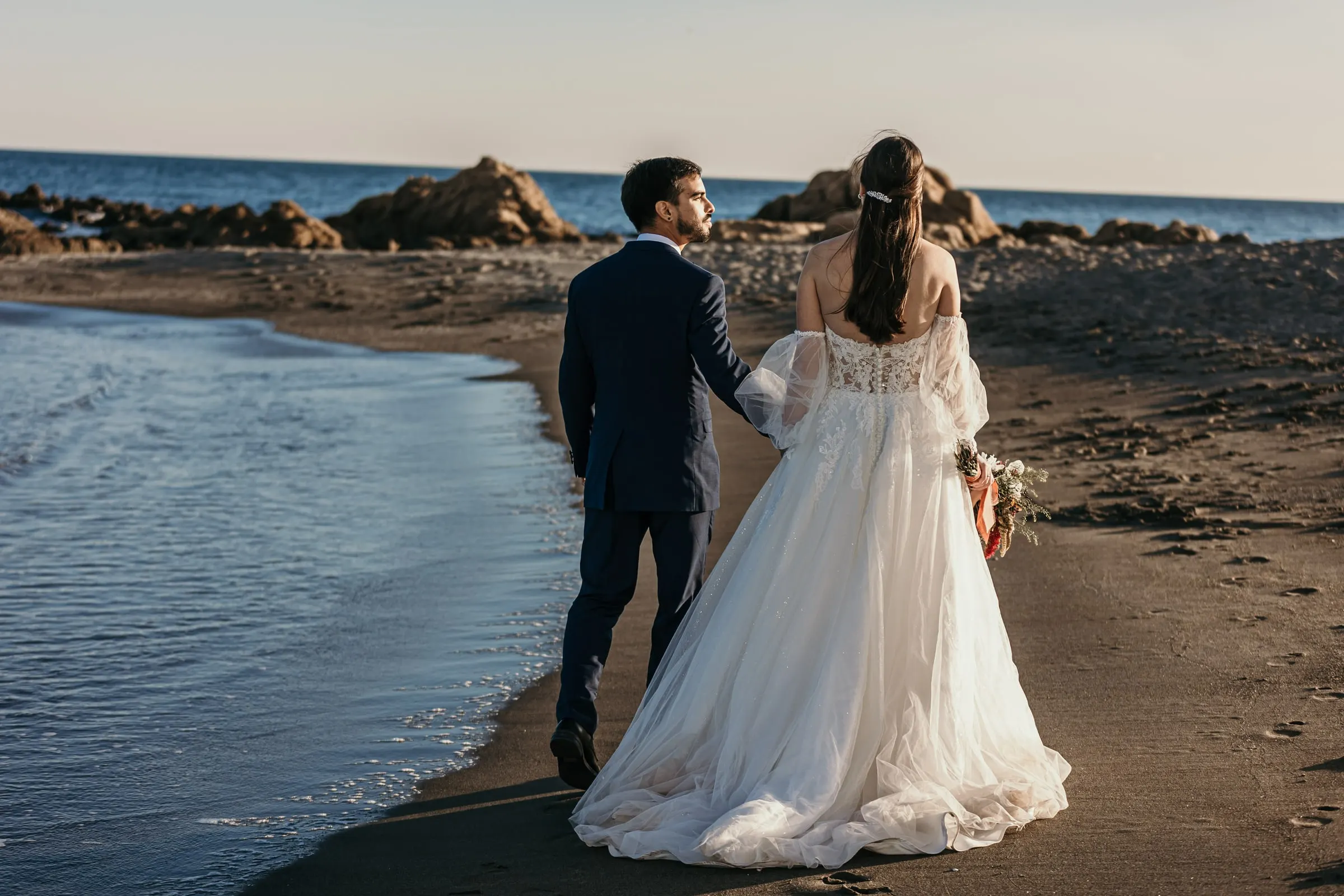 Bride and groom walking hand in hand along the shoreline, seen from behind, Cortijo San Francisco, Estepona