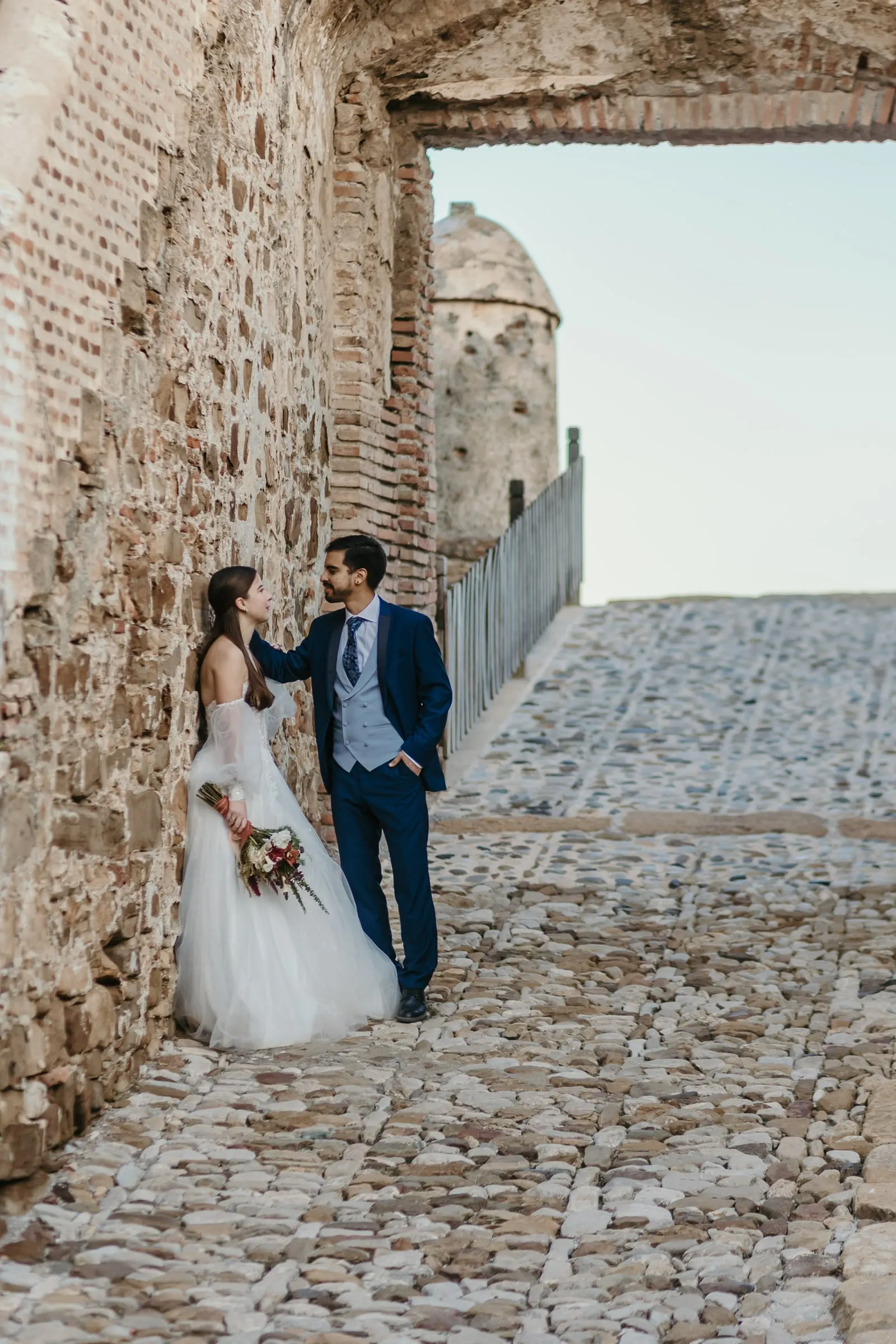 Groom leaning towards the bride against a stone wall on a cobbled ramp, Cortijo San Francisco, Estepona