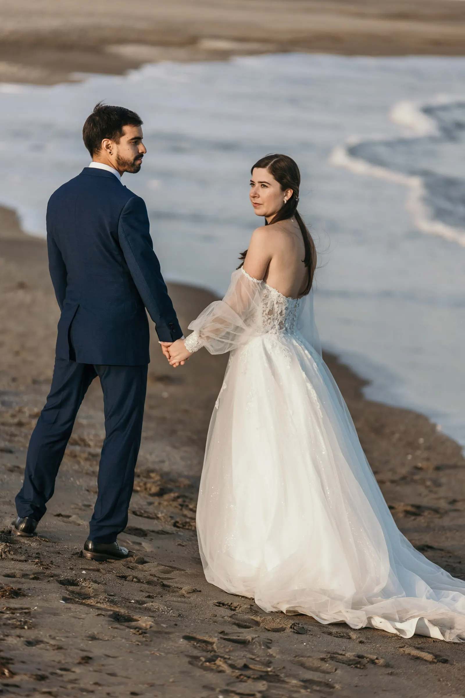 Couple holding hands on the sand as the bride looks back over her shoulder, Cortijo San Francisco, Estepona