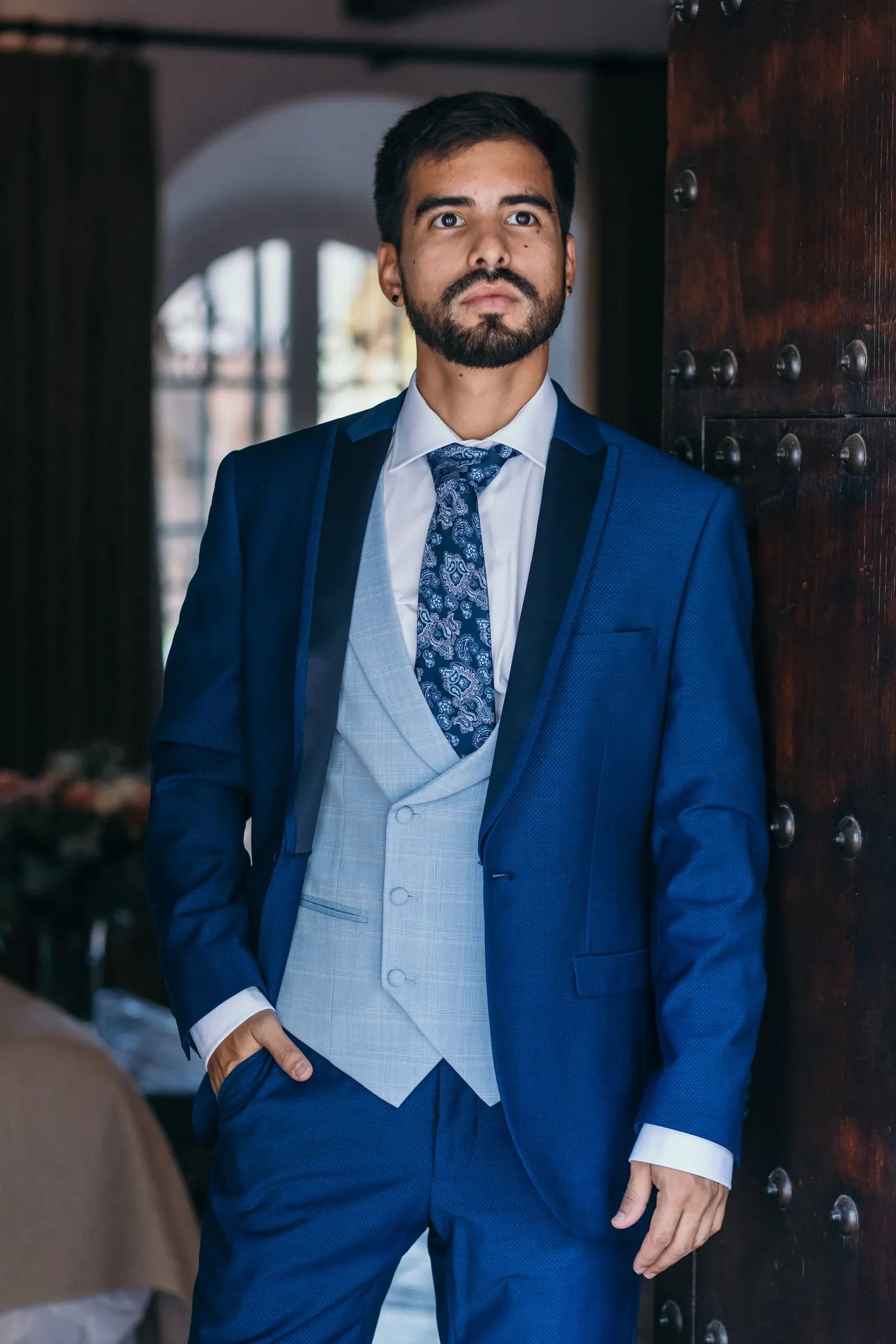 Groom posing in his navy suit and grey waistcoat by a studded wooden door, Cortijo San Francisco, Estepona