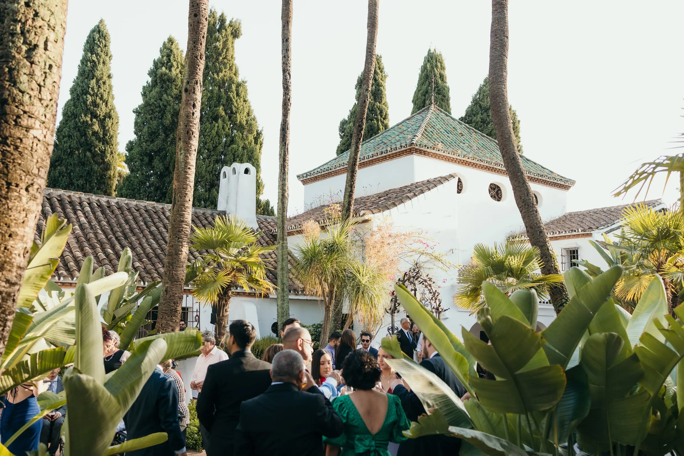 Guests gathered in a tropical garden in front of the white chapel, Cortijo San Francisco, Estepona