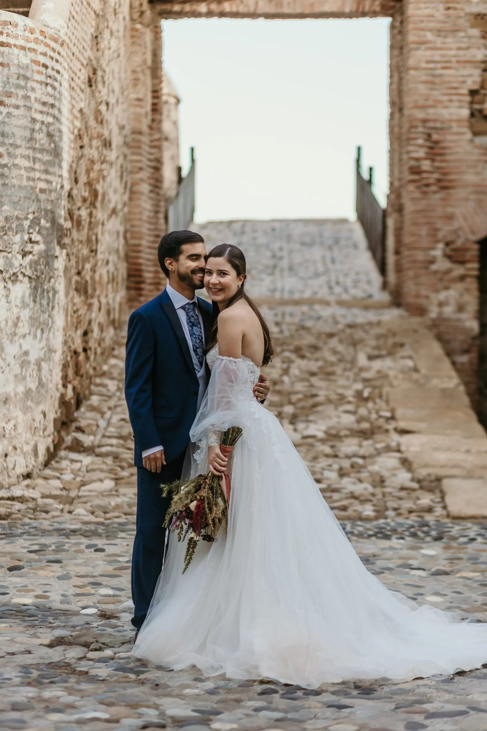 Couple embracing and smiling on a cobbled path between old walls, Cortijo San Francisco, Estepona