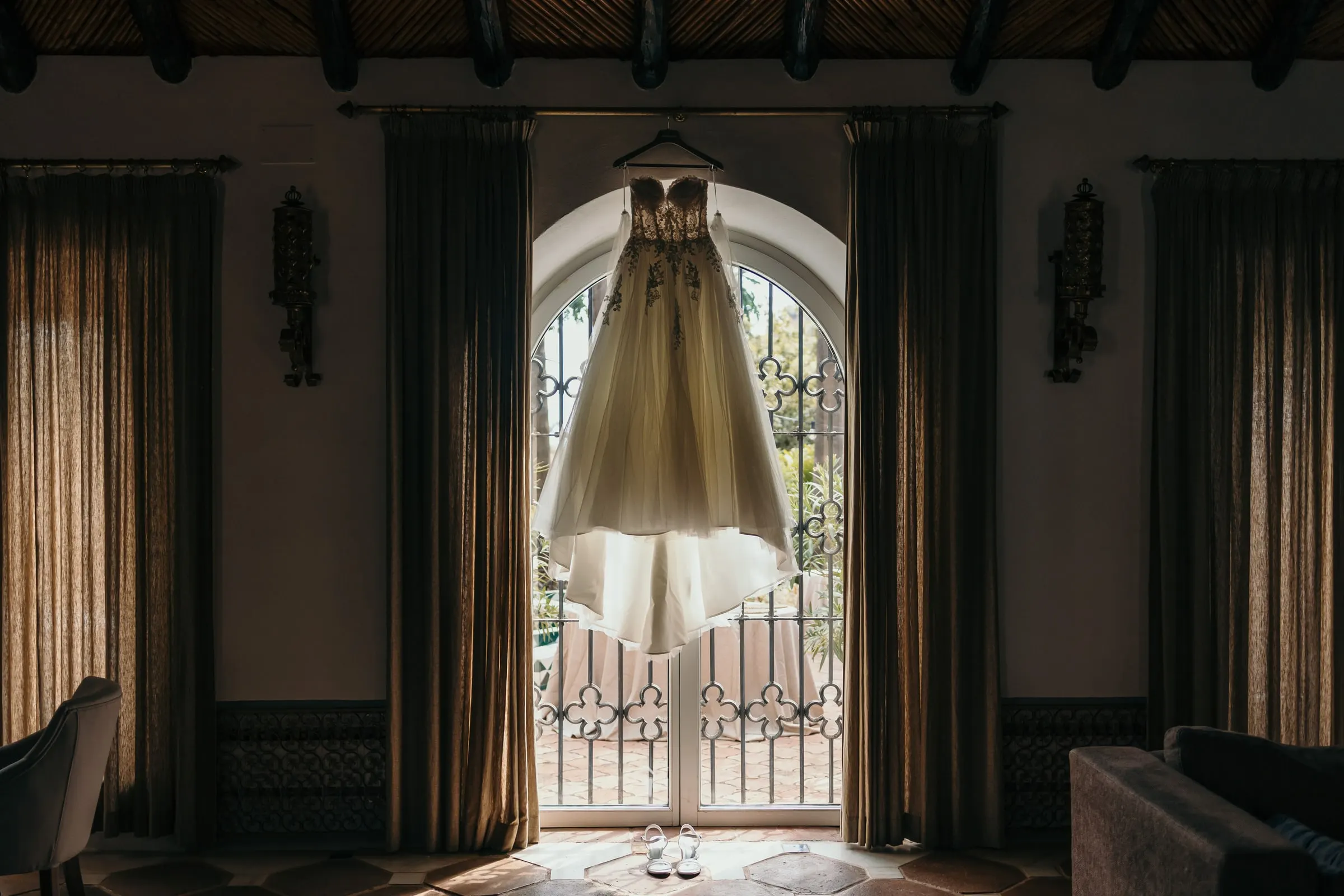 Wedding dress hanging in an arched window between heavy curtains, Cortijo San Francisco, Estepona