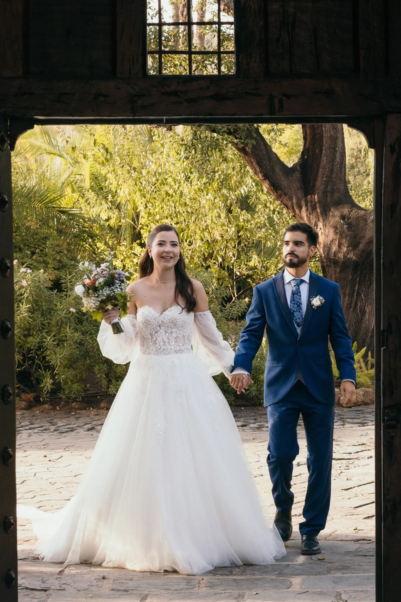 Bride and groom walking hand in hand through a wooden gateway, Cortijo San Francisco, Estepona