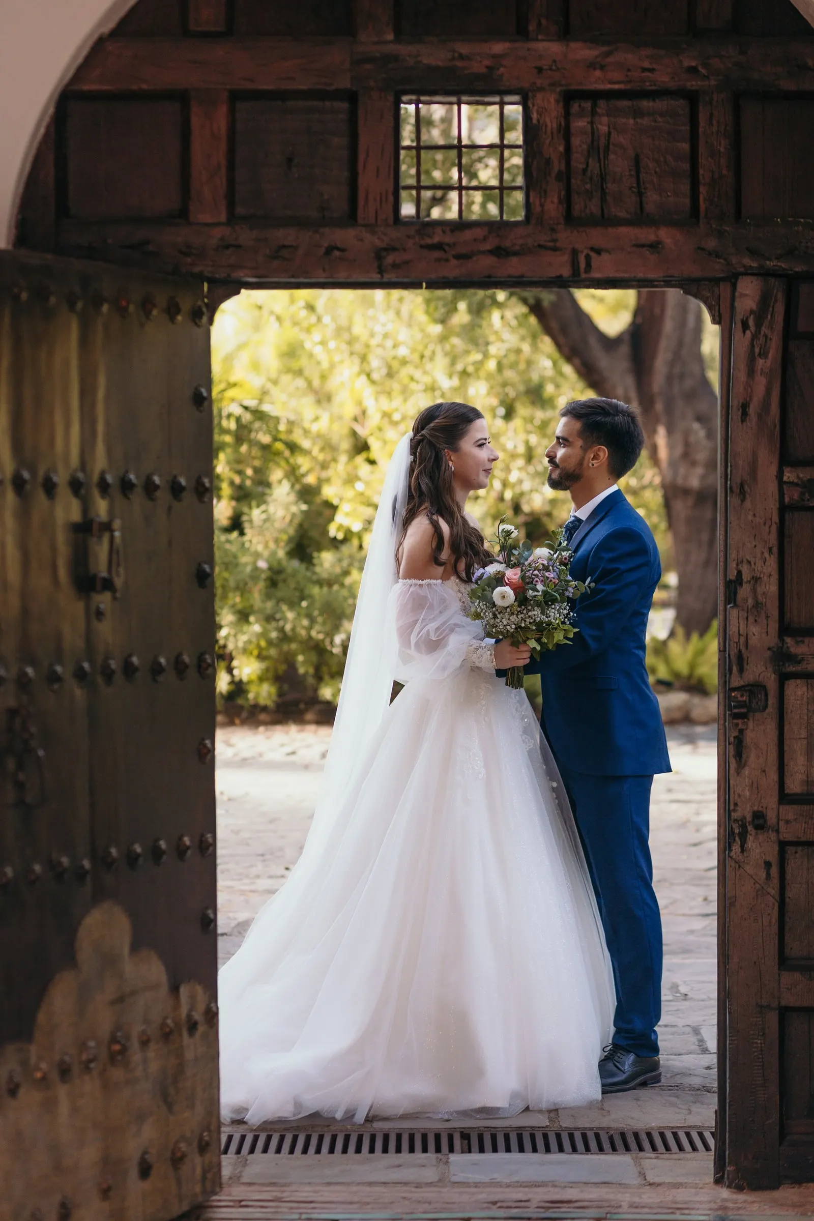 Bride and groom face to face in an open wooden doorway with greenery, Cortijo San Francisco, Estepona