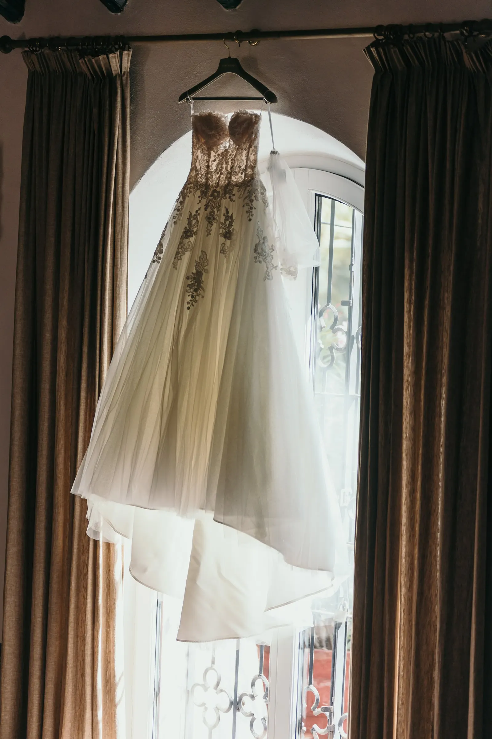 Embroidered wedding dress on a hanger against the bright window, Cortijo San Francisco, Estepona